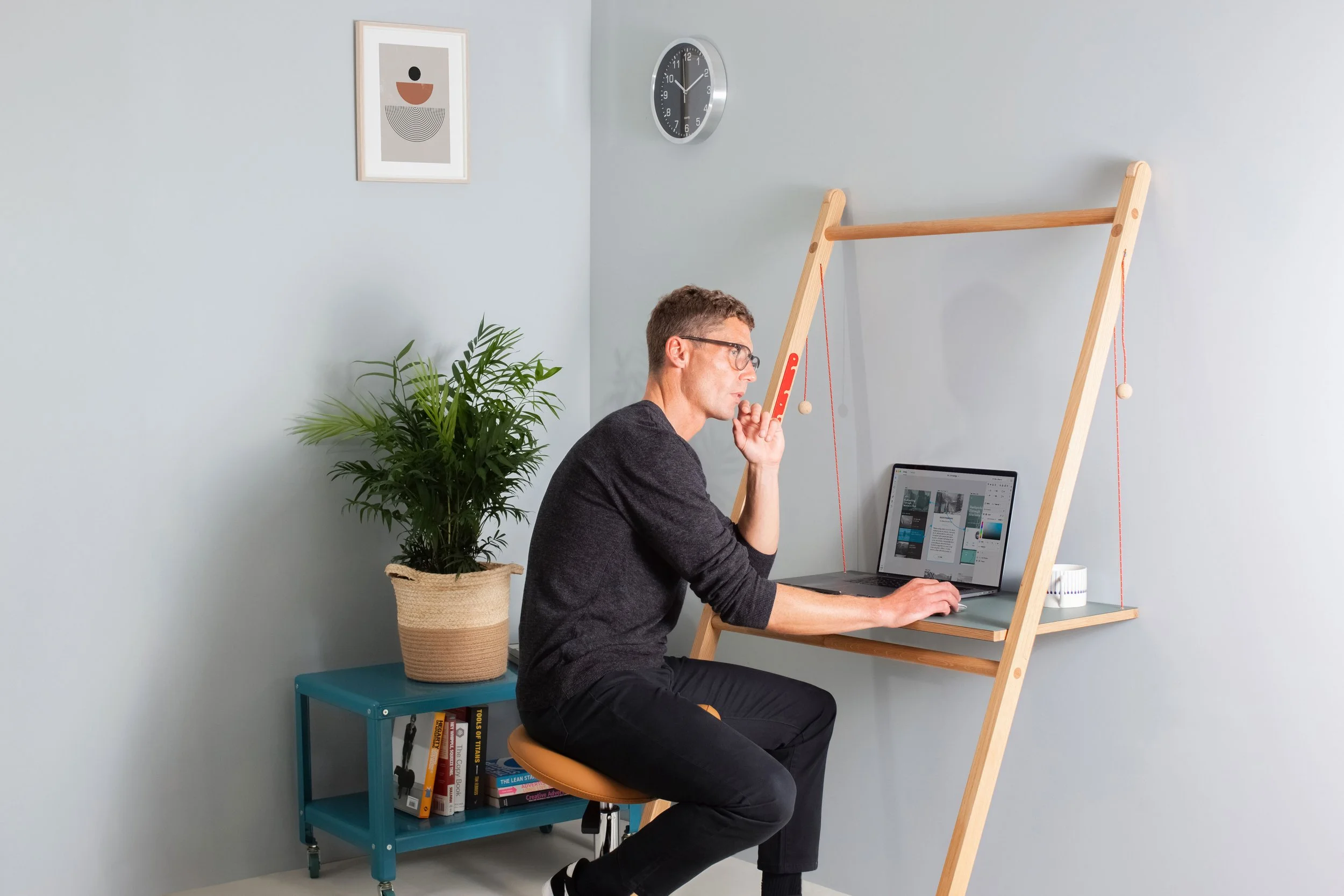 Model Matt Sharman sits at a mobile desk working on a laptop wearing glasses, a black jumper, black jeans and Vans trainers for Leandesk 