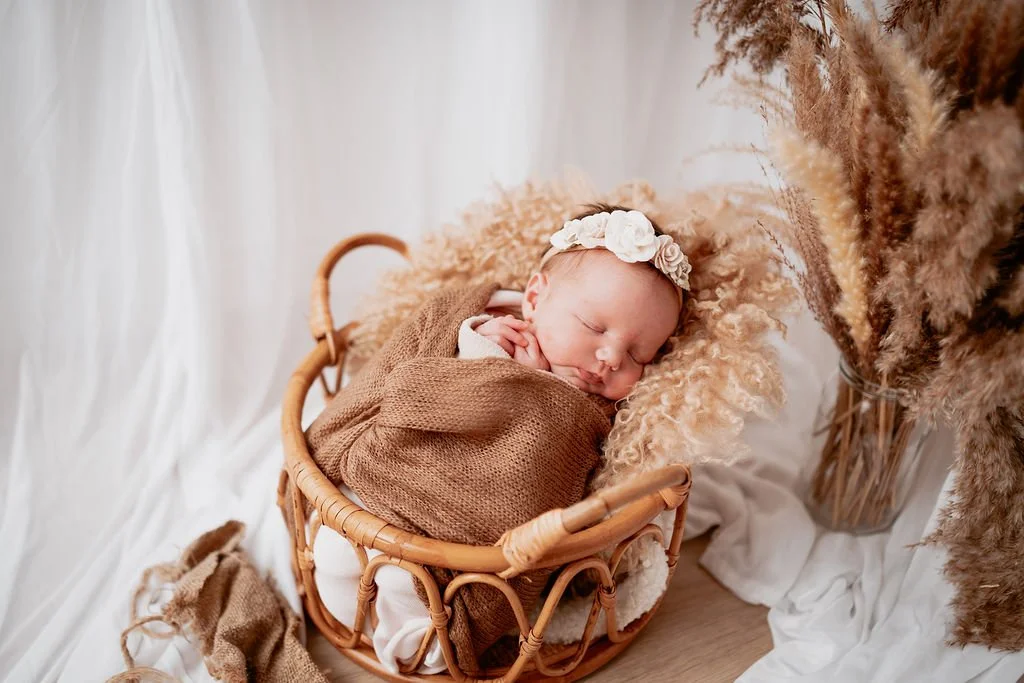 A newborn baby asleep in a basket during an autumn newborn photoshoot