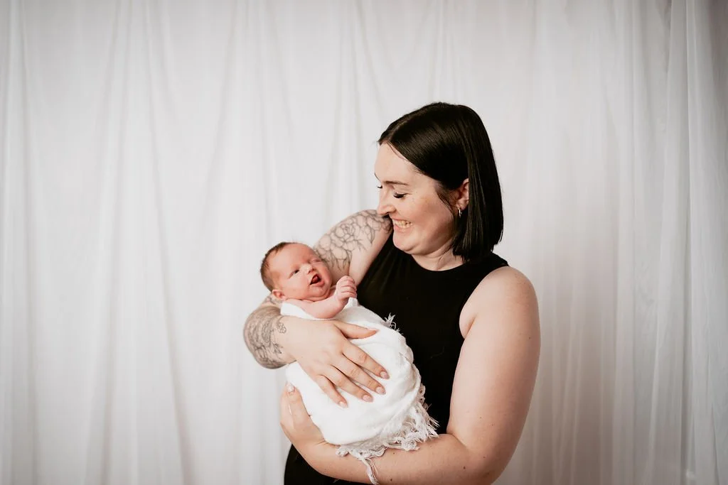 Mother smiling while holding her newborn baby during a photoshoot.