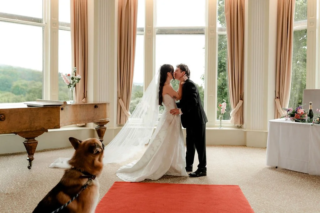 Bride and groom kissing beneath colourful wedding flowers inside Atholl Palace Hotel, Pitlochry.