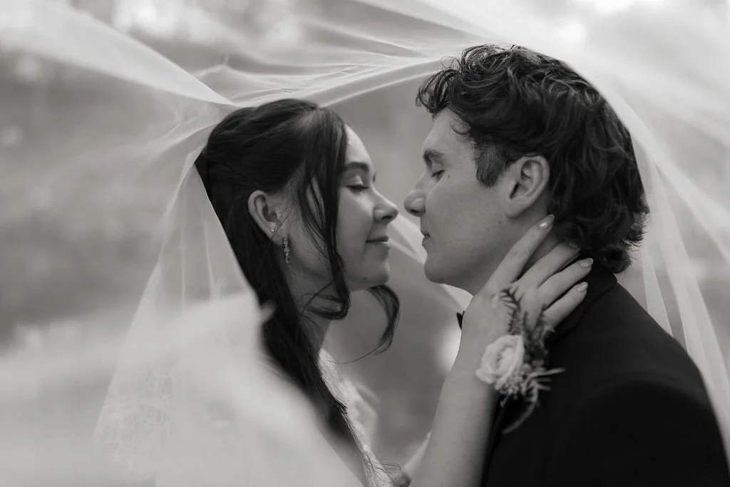 Close-up black-and-white portrait of the bride embracing the groom beneath her flowing wedding veil.