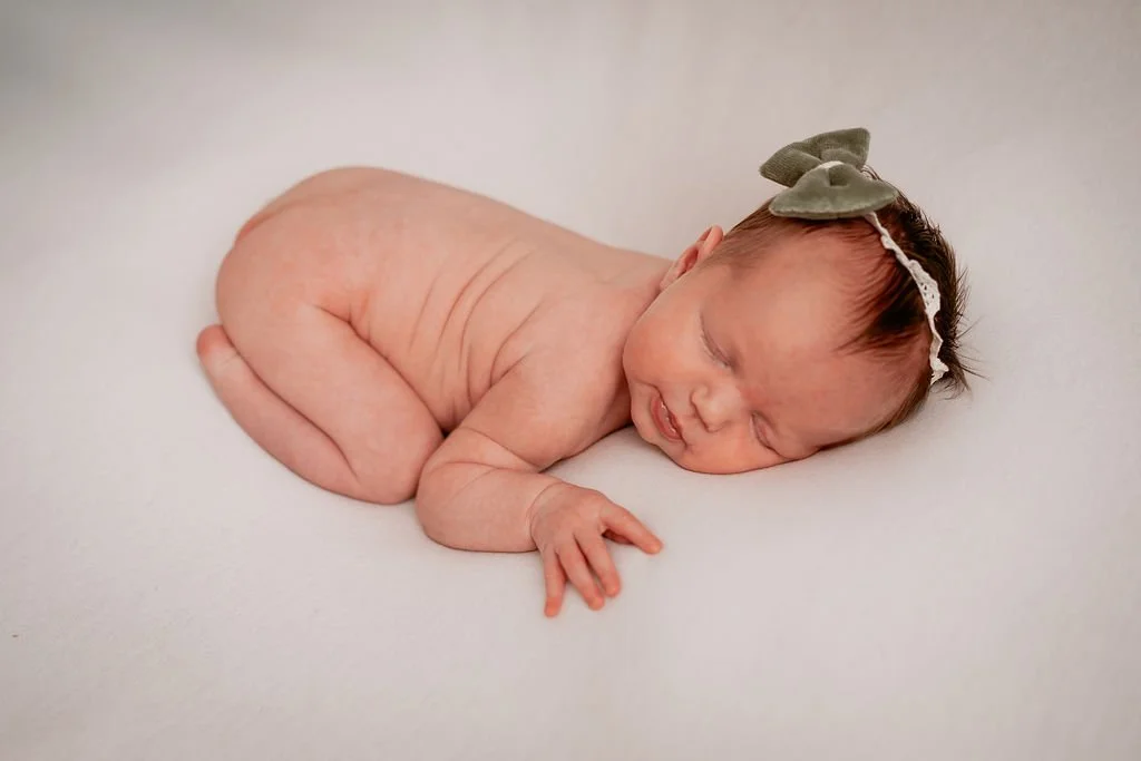 A newborn baby wearing a bow captured in soft, natural light
