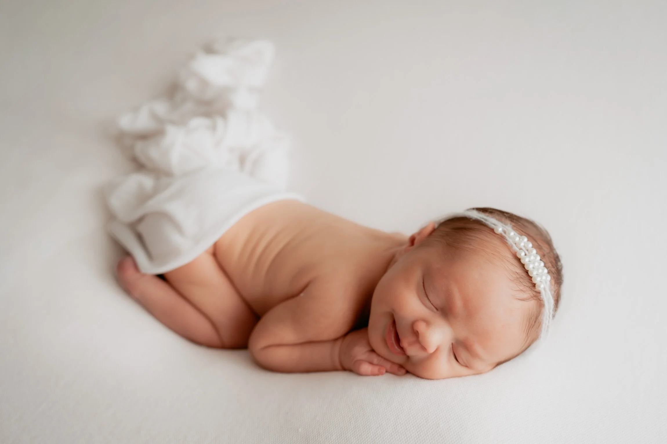 Close-up newborn portrait of baby Maya sleeping in a cream lace outfit with a delicate neutral flower headband.