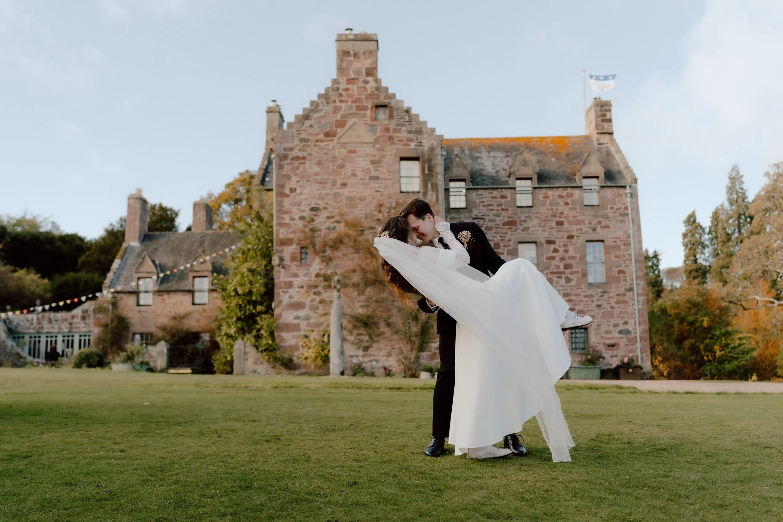 Married couple going for a dip-kiss in front of walled garden Rufflets Hotel in St Andrews. A picture from a fairytaile scottish wedding