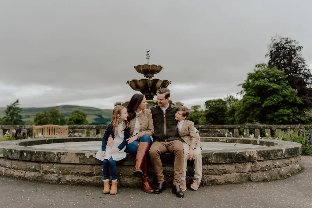 Family sitting together beside the fountain during their Gleneagles family photography experience in Scotland captured by Patrice Little Photography