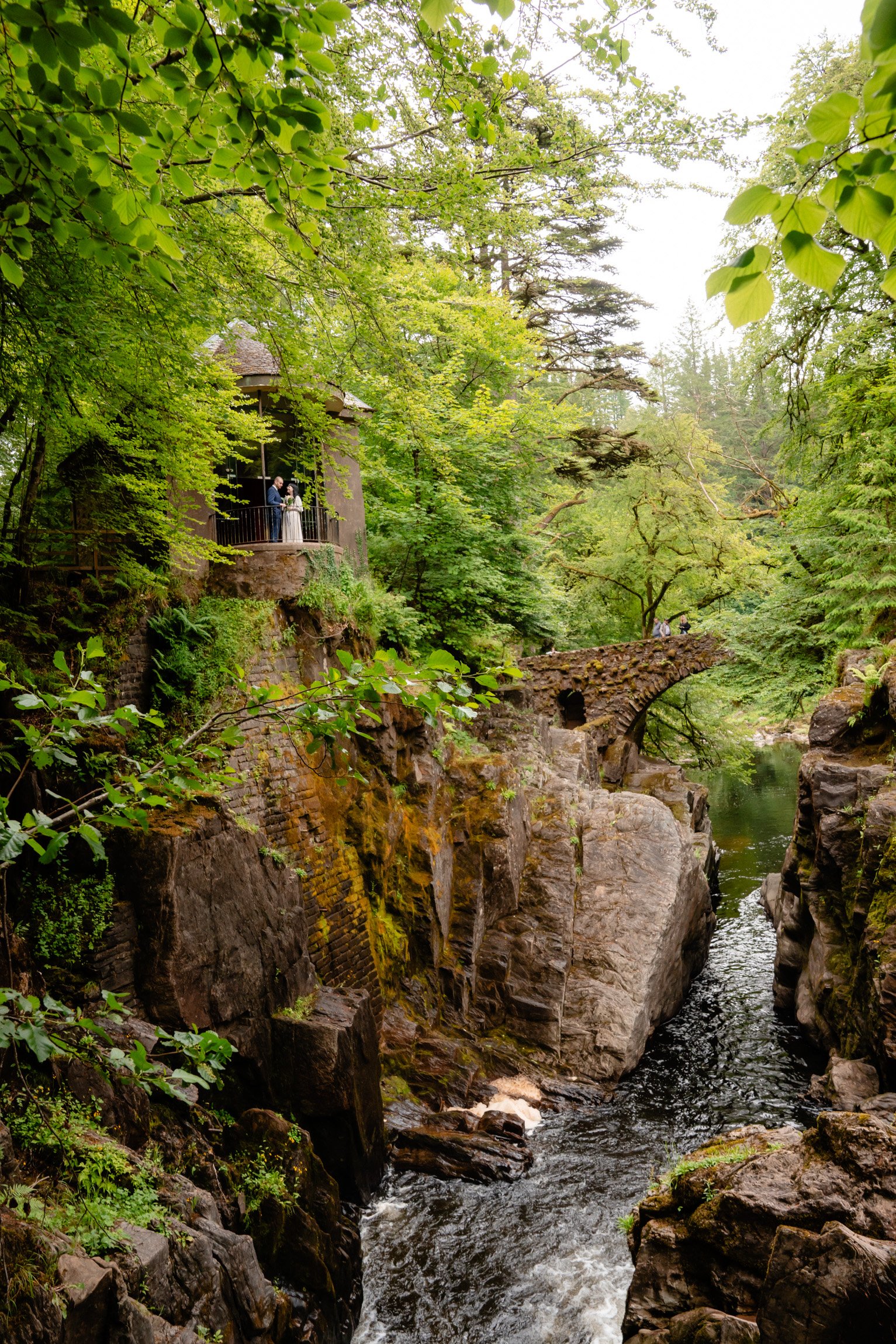 Couple standing outside a woodland cottage above the river at The Hermitage, Scotland