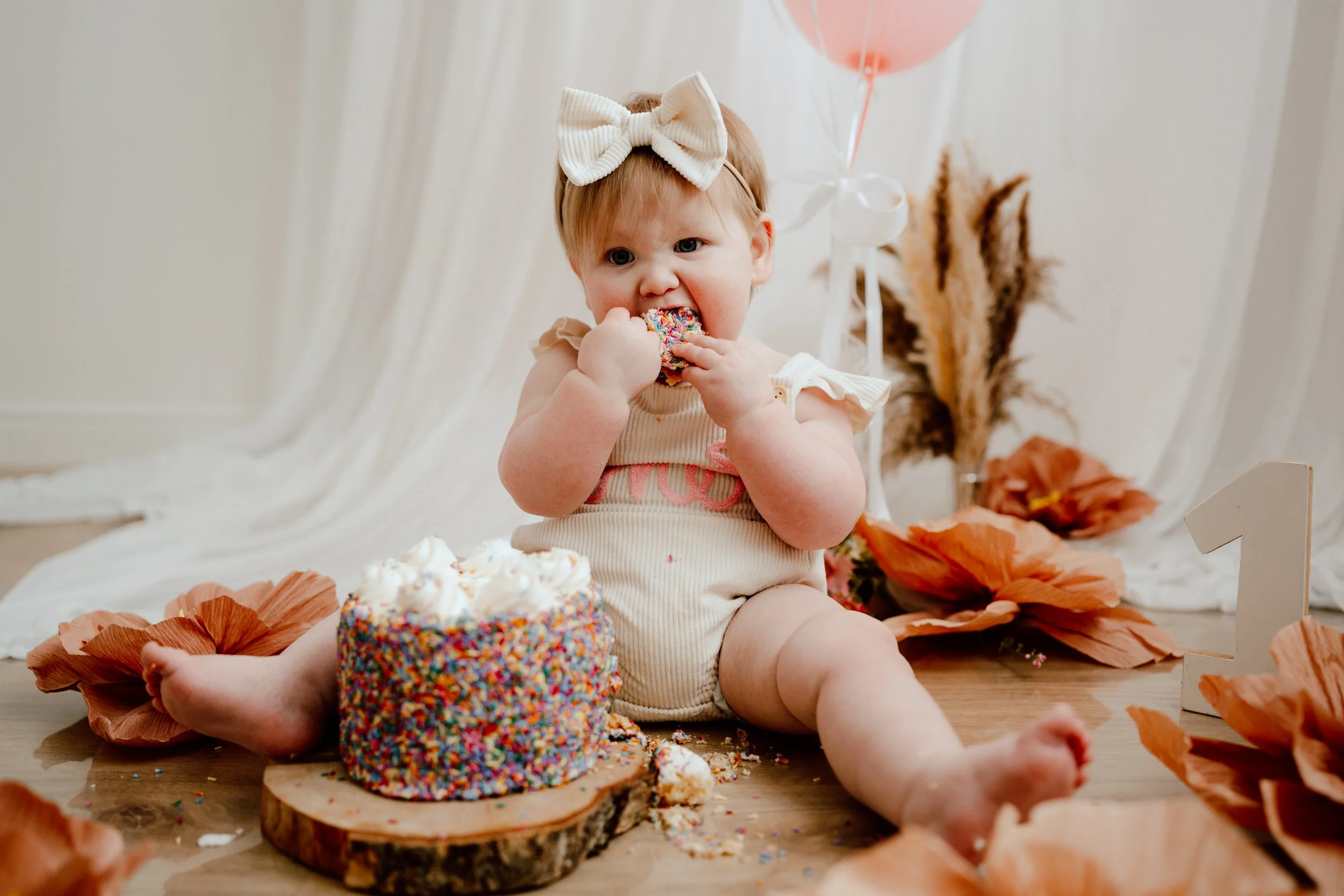 Toddler in pink outfit enjoying piece of cake at their cake smash photoshoot in studio in Perthshire