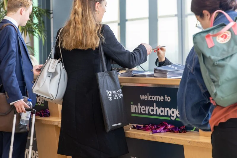 People at a university exchange program registration desk, with a sign that reads "welcome to interchange."