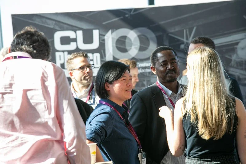 People engaged in conversation at a professional event with a banner reading 'CU 100' in the background.