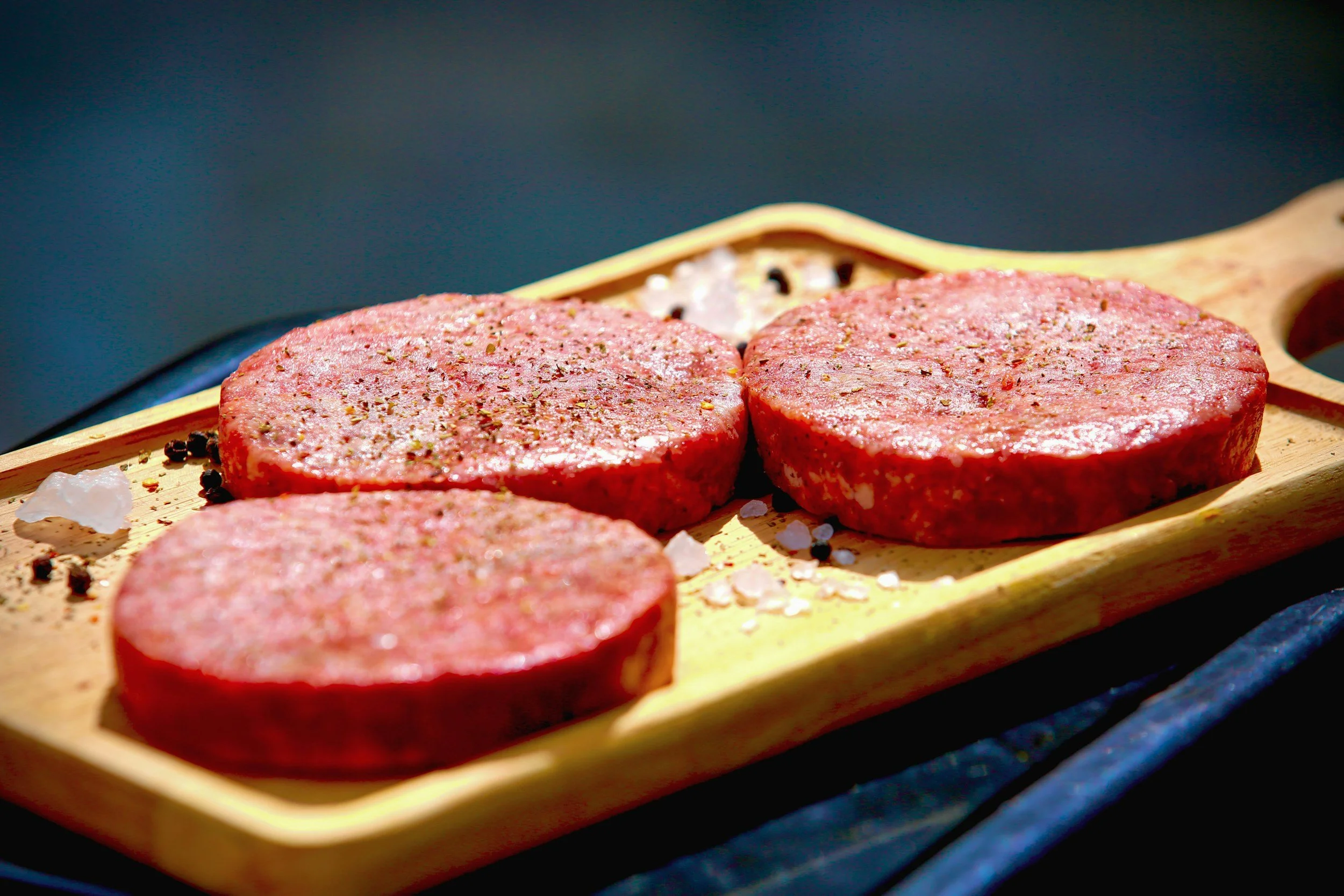 Three raw burger patties on a wood cutting board