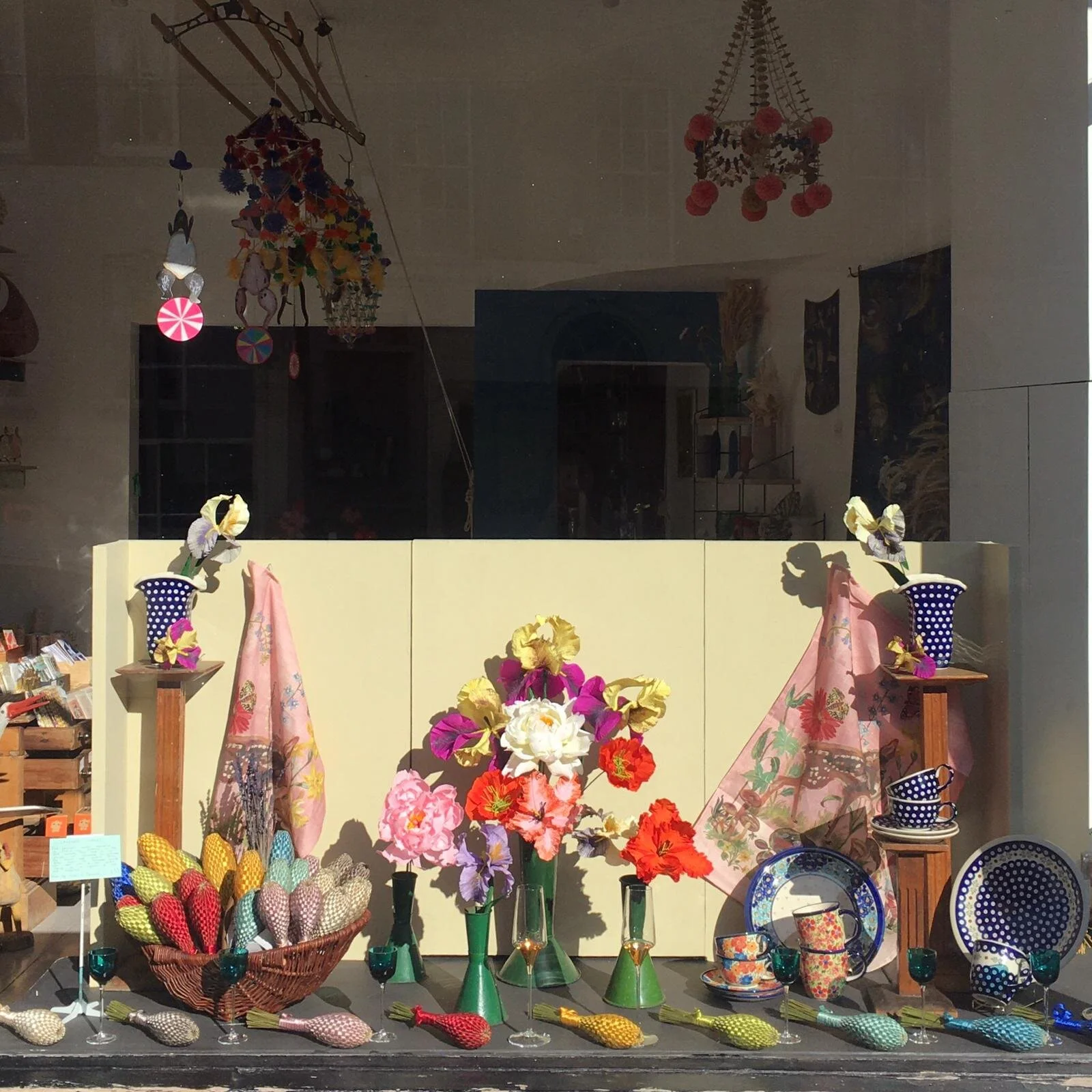 Display of colorful ceramics, paper flowers by Emmeli Kimhi, and textiles in a shop window showcase.