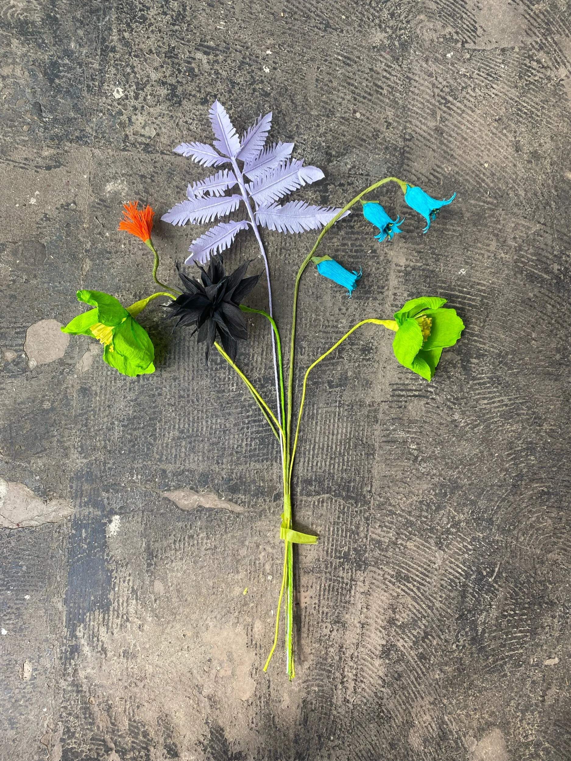 Colorful artificial flowers by Emmeli Kimhi and leaves arranged on the ground.