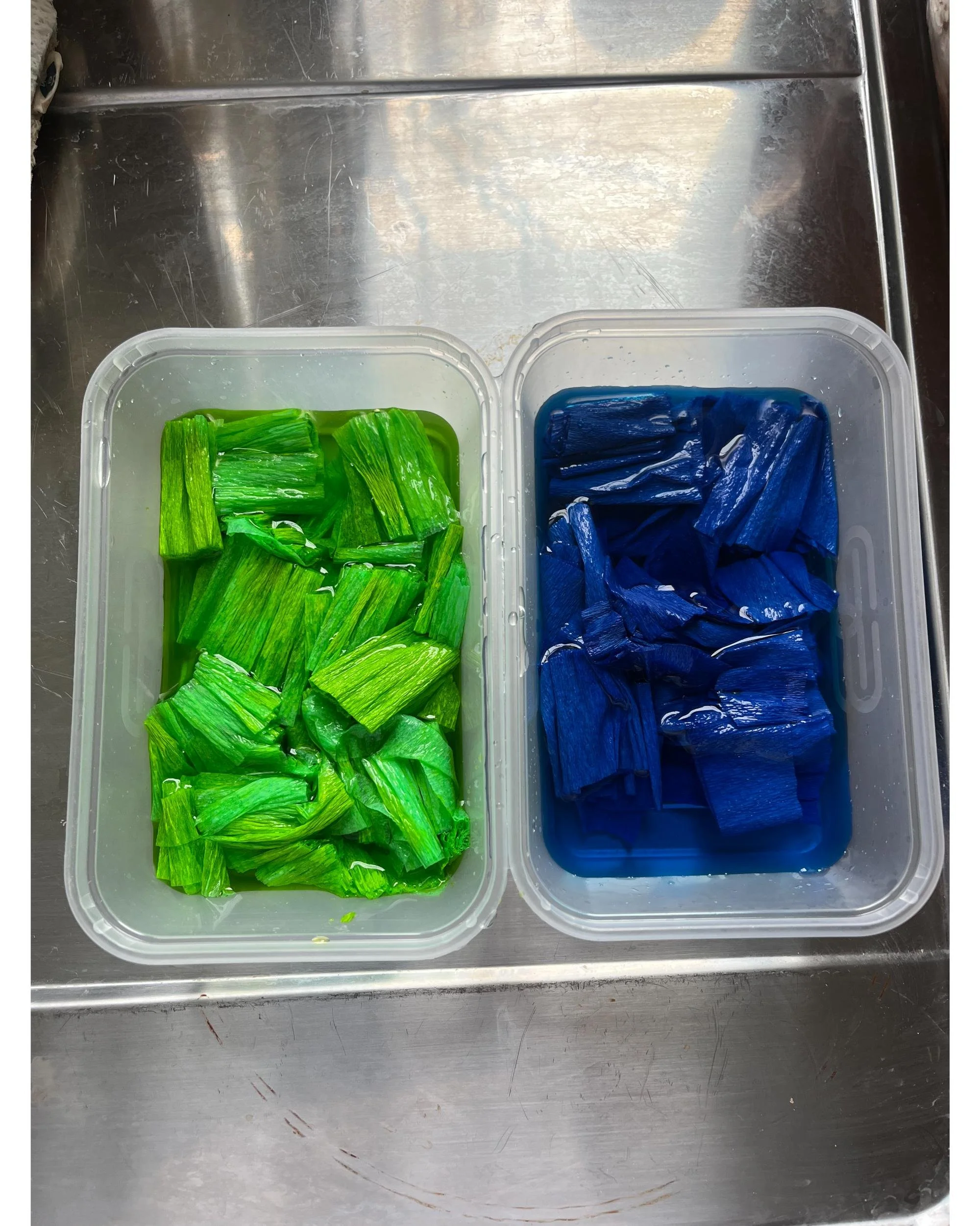 Bright green and deep blue crepe paper strips soaking in dye baths, part of the hand-dyeing process in Emmeli Kimhi’s London studio