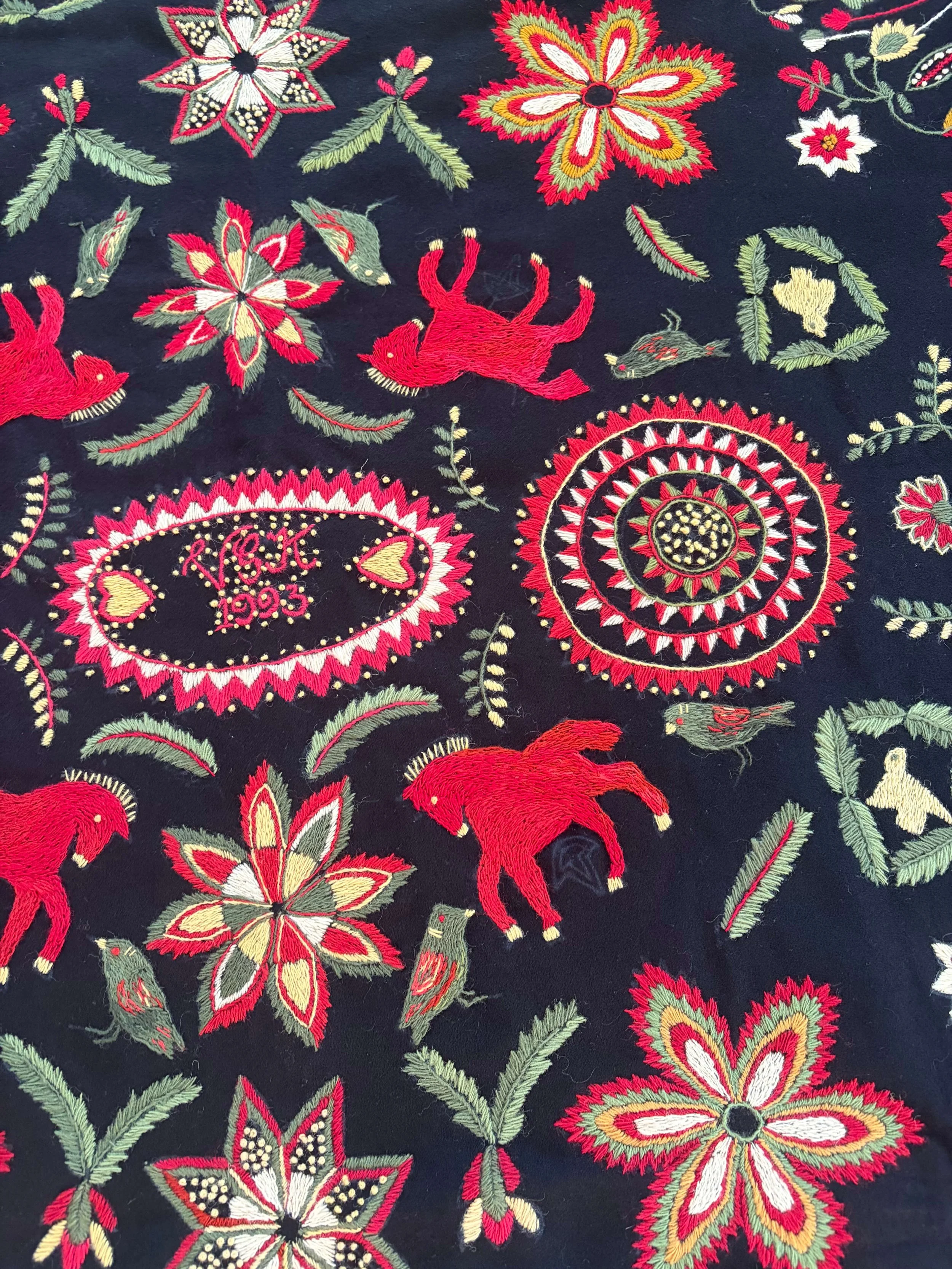 Close-up of a skånsk yllebroderi wool embroidery showing embroidered horses, a bird, a circular medallion, and an oval with initials and the date 1993