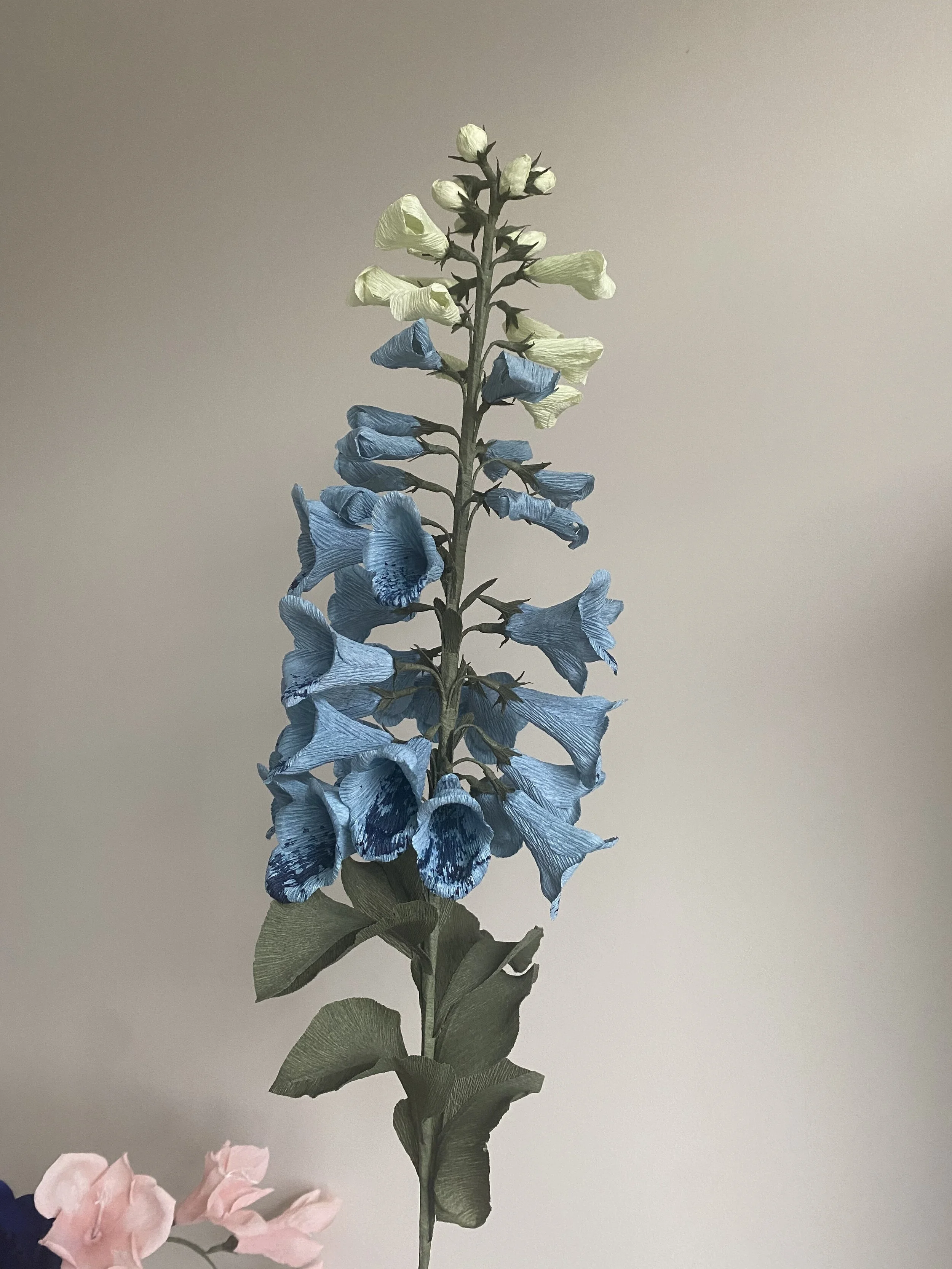 Artificial flower stem with blue, yellow, and pink flowers by Emmeli Kimhi against a plain background.