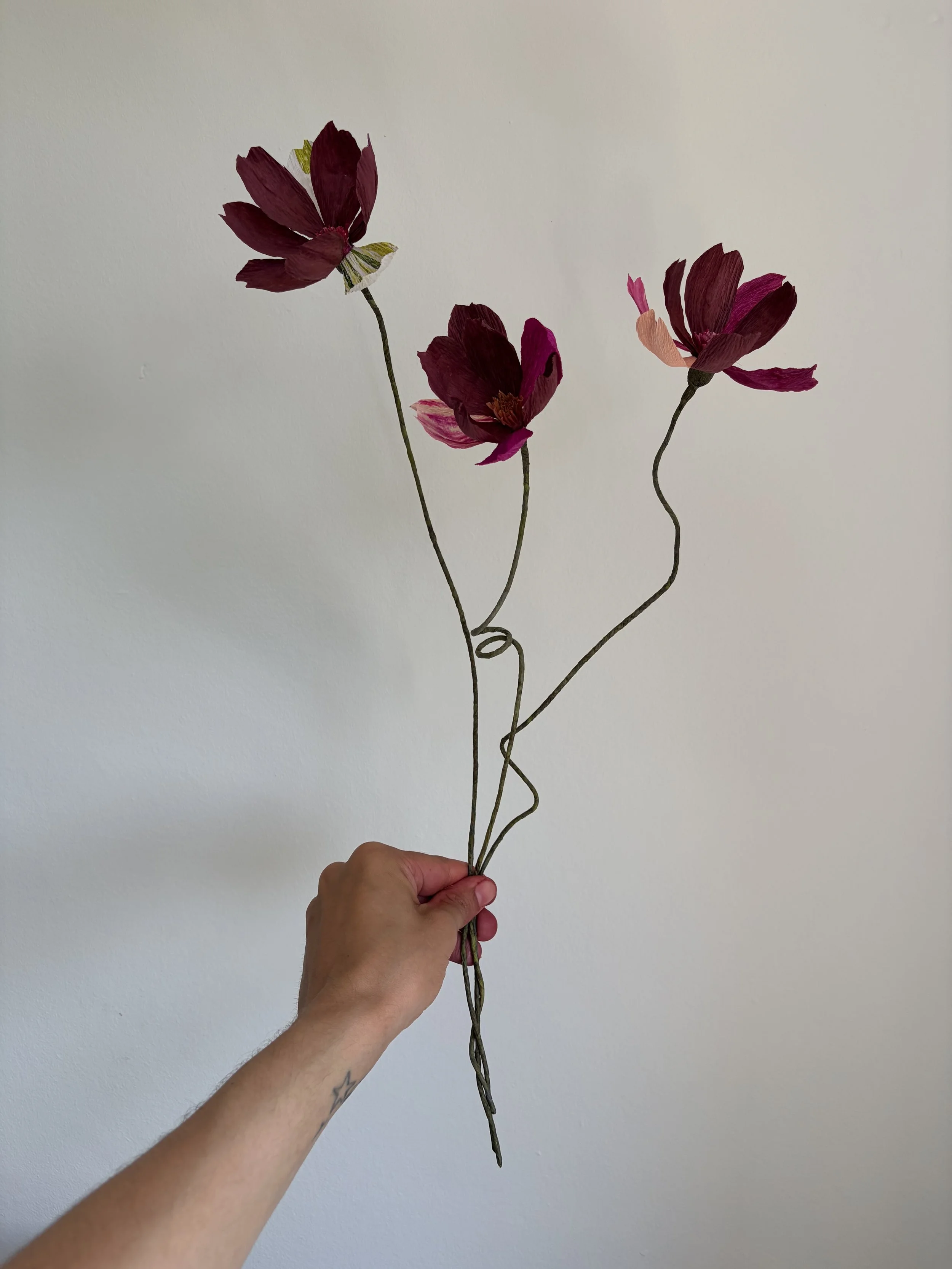 Three handmade paper cosmos flowers in rich plum and magenta tones with whimsical wired stems. Bespoke paper flowers created for Studio Duggan’s SpeakEasy Salon at WOW!house 2026.