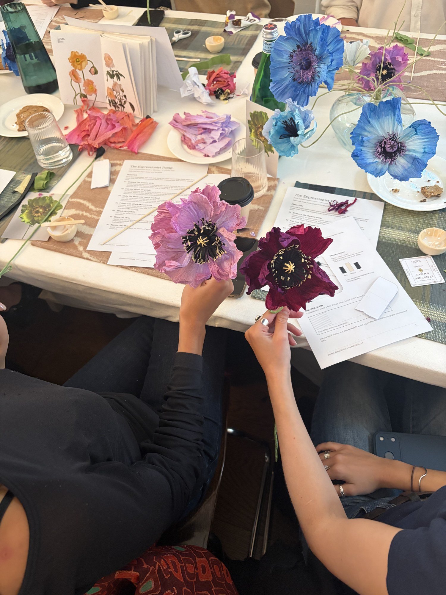 Two guests holding finished paper poppies in pink and deep plum