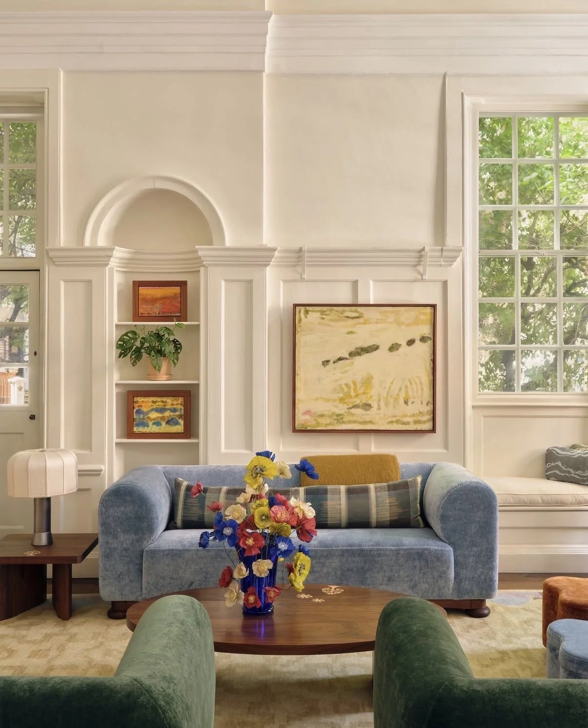 Emmeli Kimhi paper poppies in a cobalt vase at SISTER by Studio Ashby, set on a round wood coffee table between green velvet armchairs and a pale blue sofa.