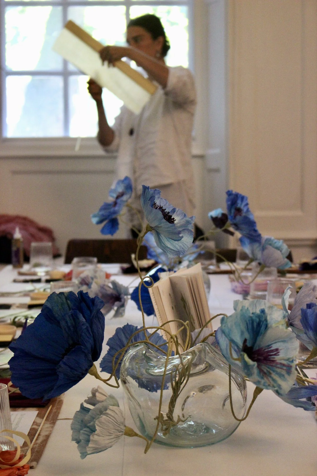 Blue crepe paper poppies in a clear glass vase on the workshop table