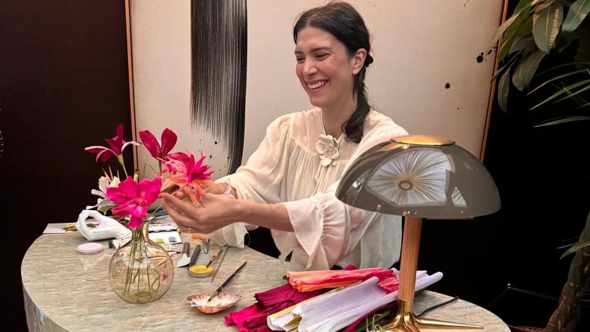 Emmeli Kimhi smiling while holding a vibrant pink paper cosmos flower during her live demonstration for Studio Duggan’s SpeakEasy Salon at WOW!house 2026.
