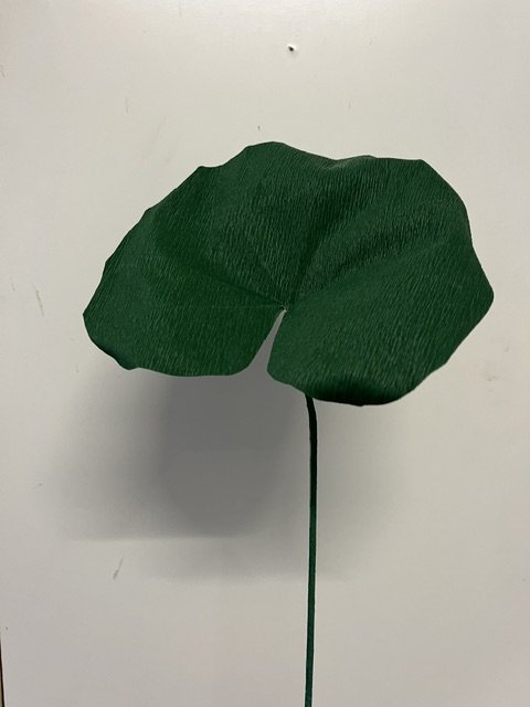 Artificial green leaf by Emmeli Kimhi on a black wire stem against a plain white background.