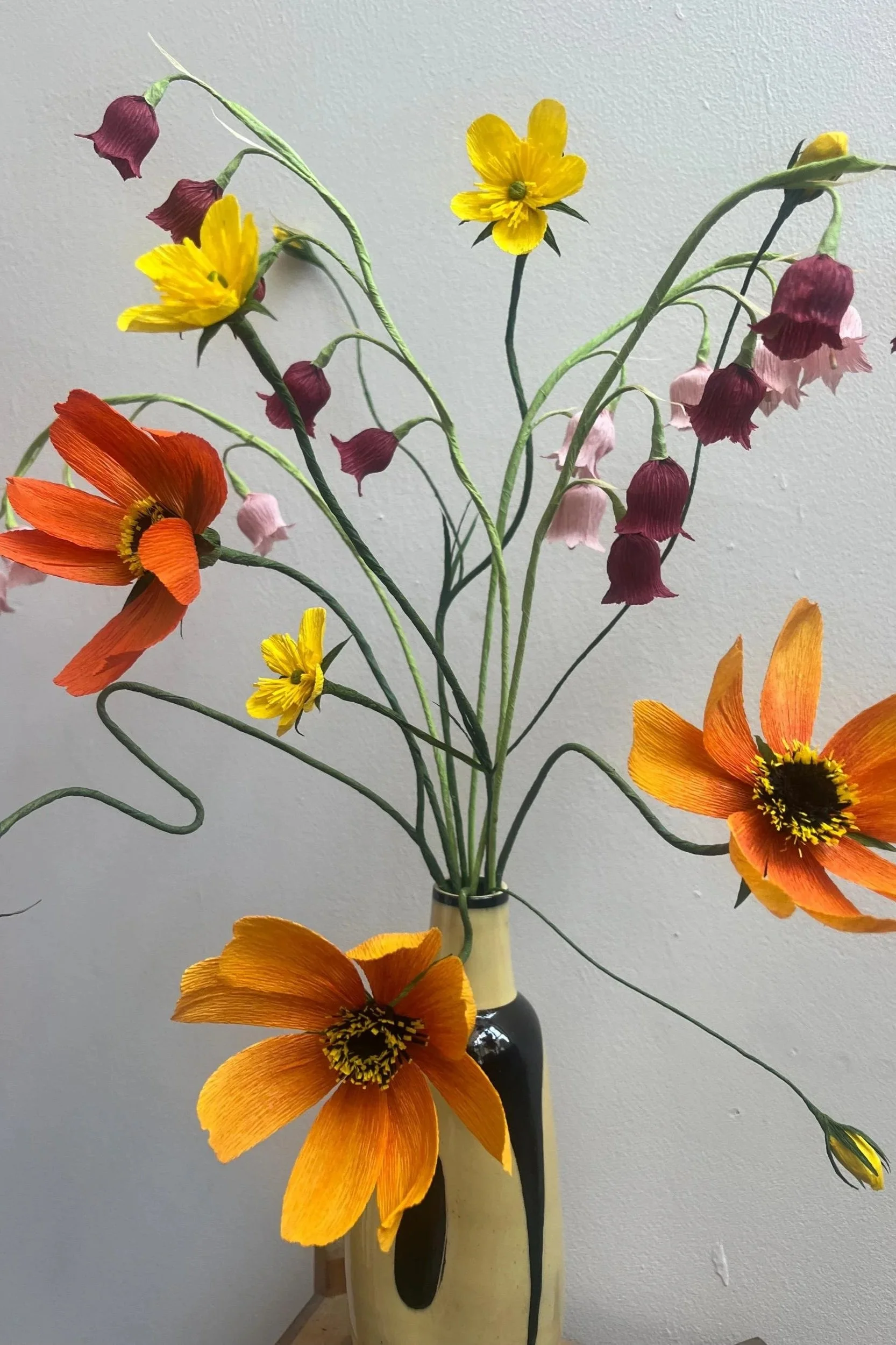 Detailed view of handmade paper flowers featuring a vibrant orange cosmos and deep purple bell-shaped blooms by Emmeli Kimhi