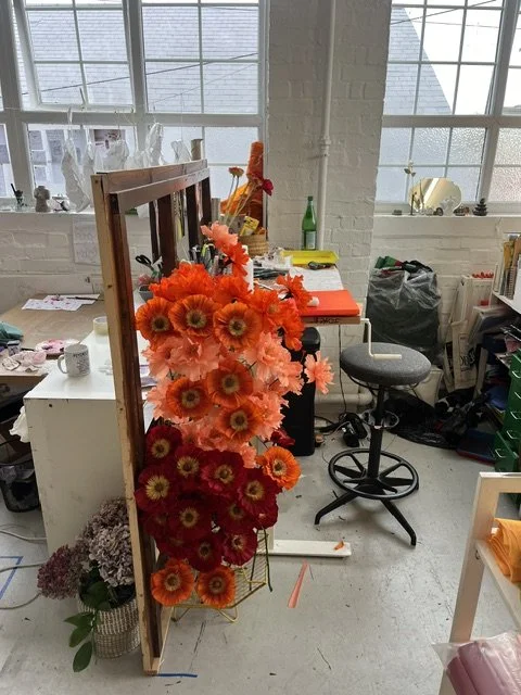 A wooden stand with orange and red artificial flowers in Emmeli Kimhi's workshop in London.