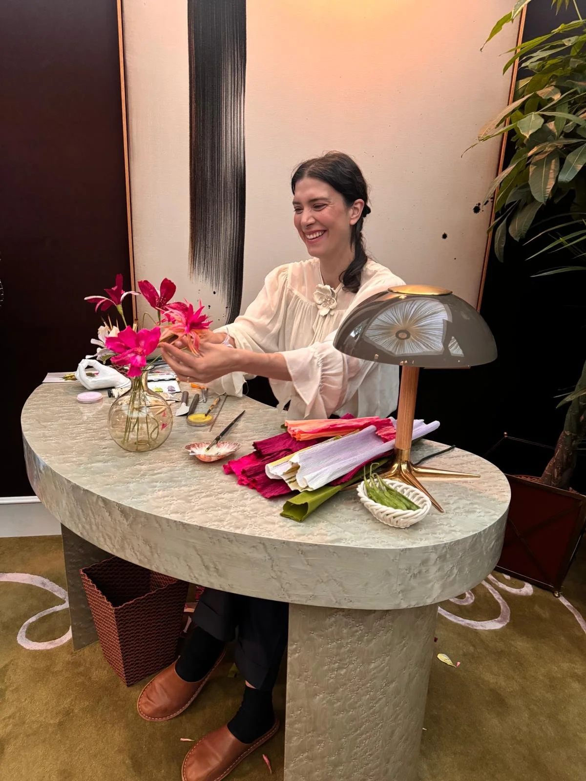 Paper flower artist Emmeli Kimhi smiling while holding a vibrant pink cosmos flower during a live demonstration for Studio Duggan at WOW!house. Handmade paper flowers created for The SpeakEasy Salon.