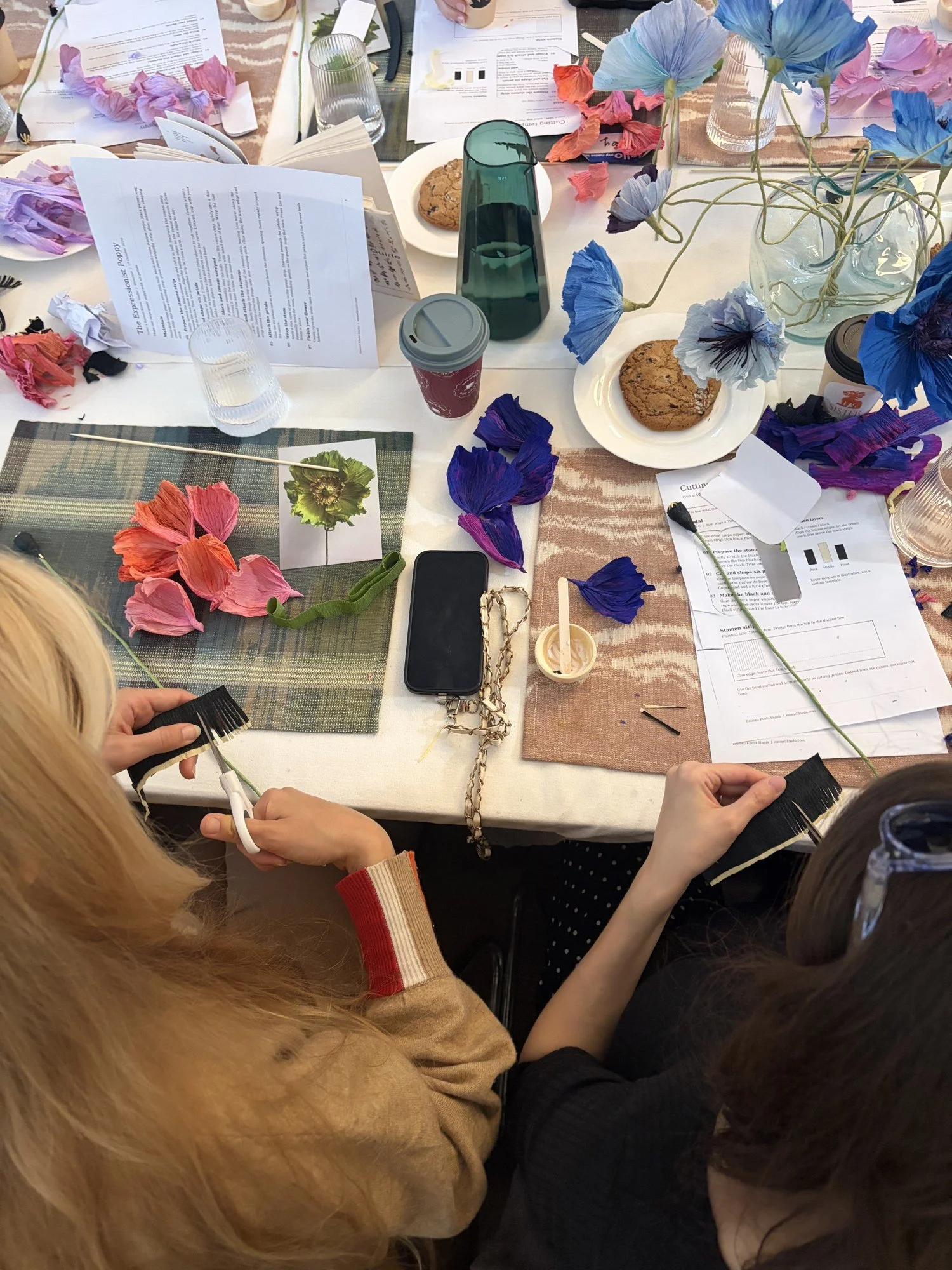 Guests cutting crepe paper petals, with finished pink, blue and red paper poppies on the table
