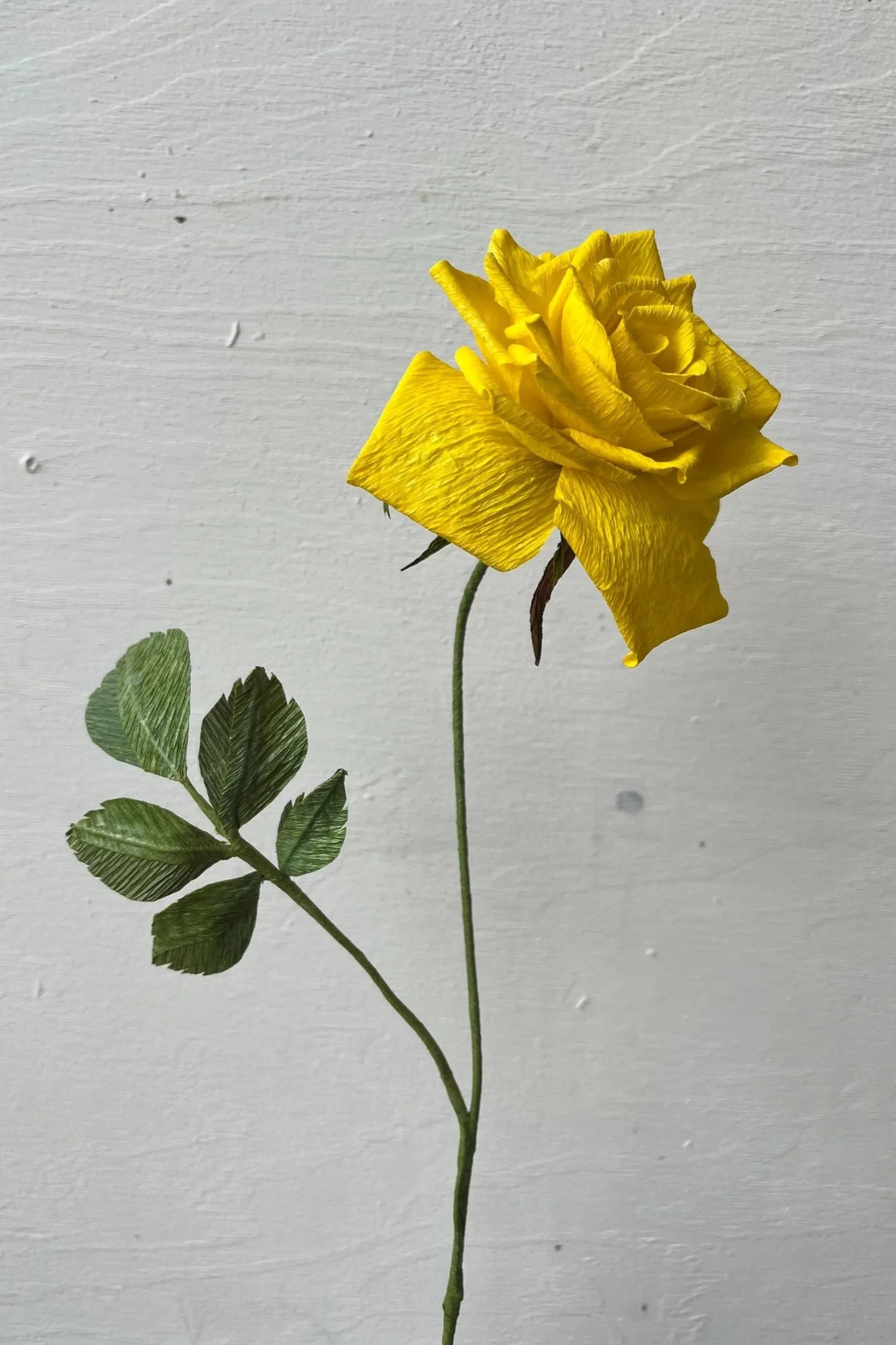 Bright yellow handmade paper rose with rich texture and green leaves by Emmeli Kimhi