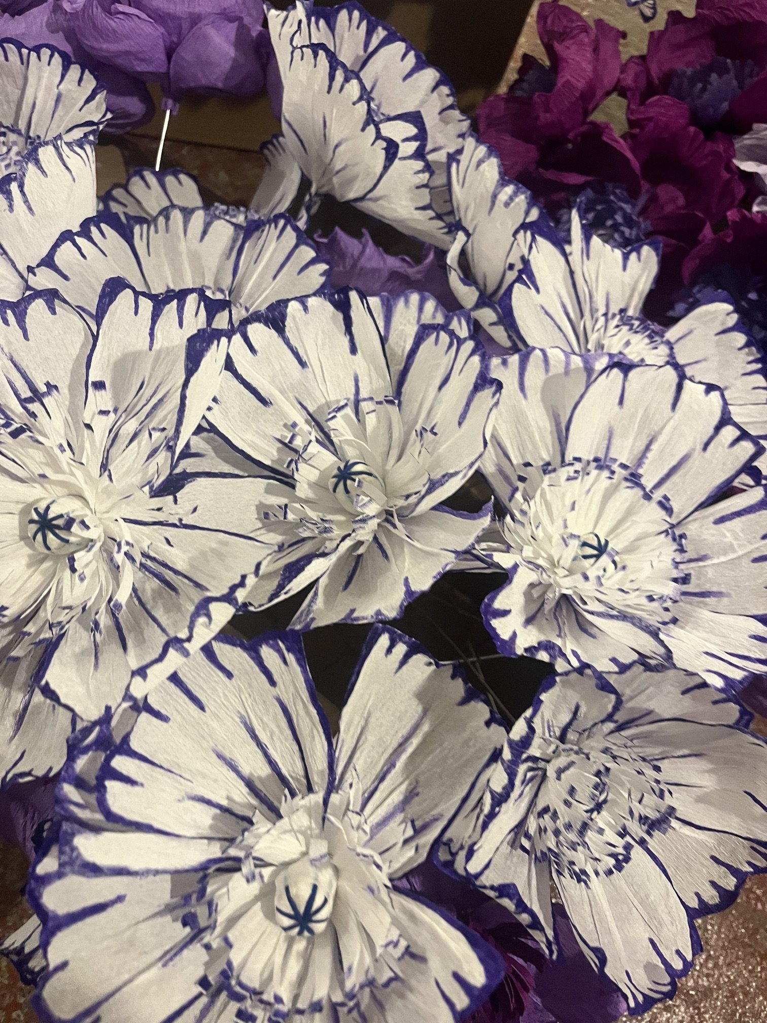 Multiple white and purple paper origami flowers by Emmeli Kimhi with blue outlines and detail.