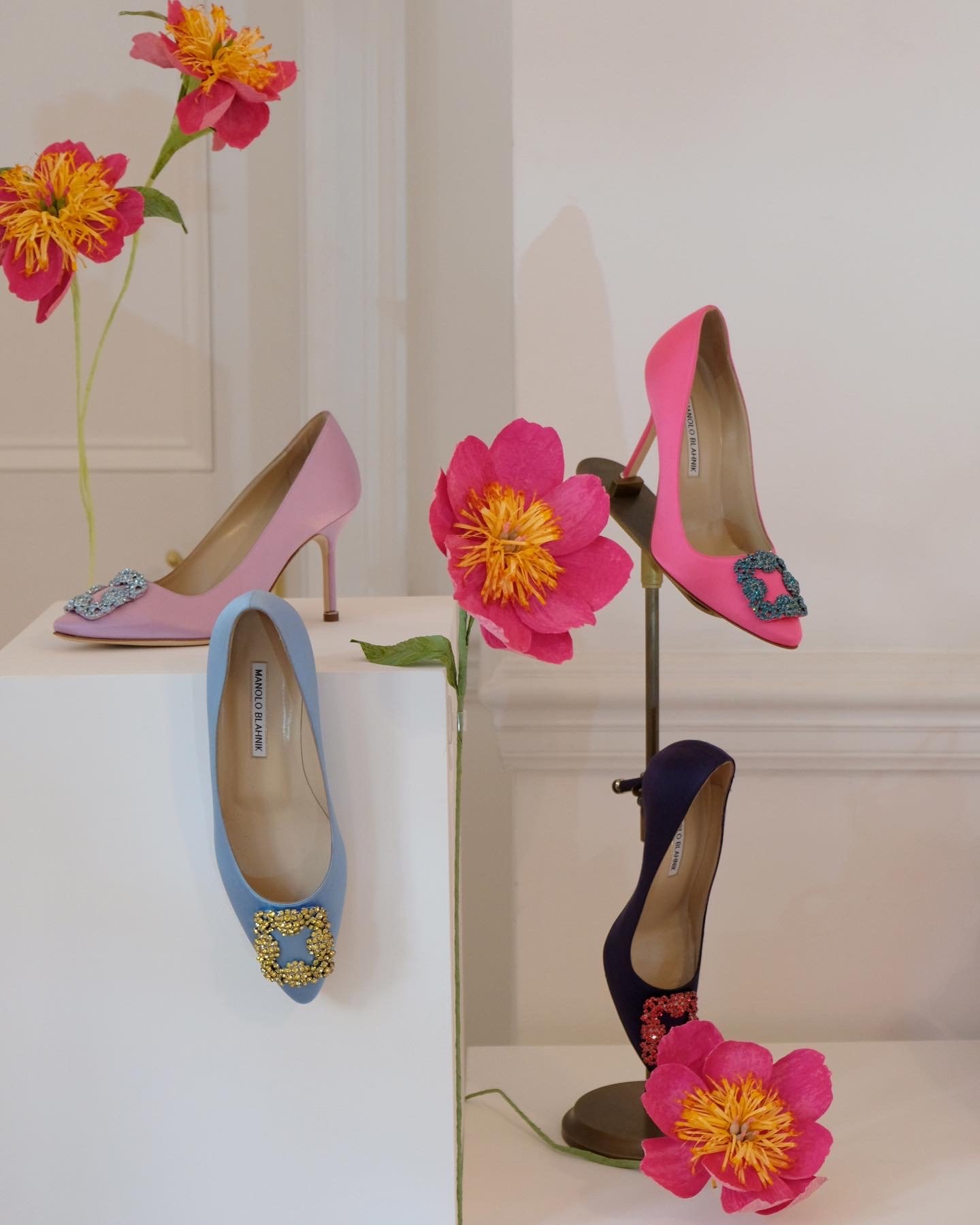 Display of four high-heeled shoes on white platforms, decorated with pink and yellow paper flowers by Emmeli Kimhi