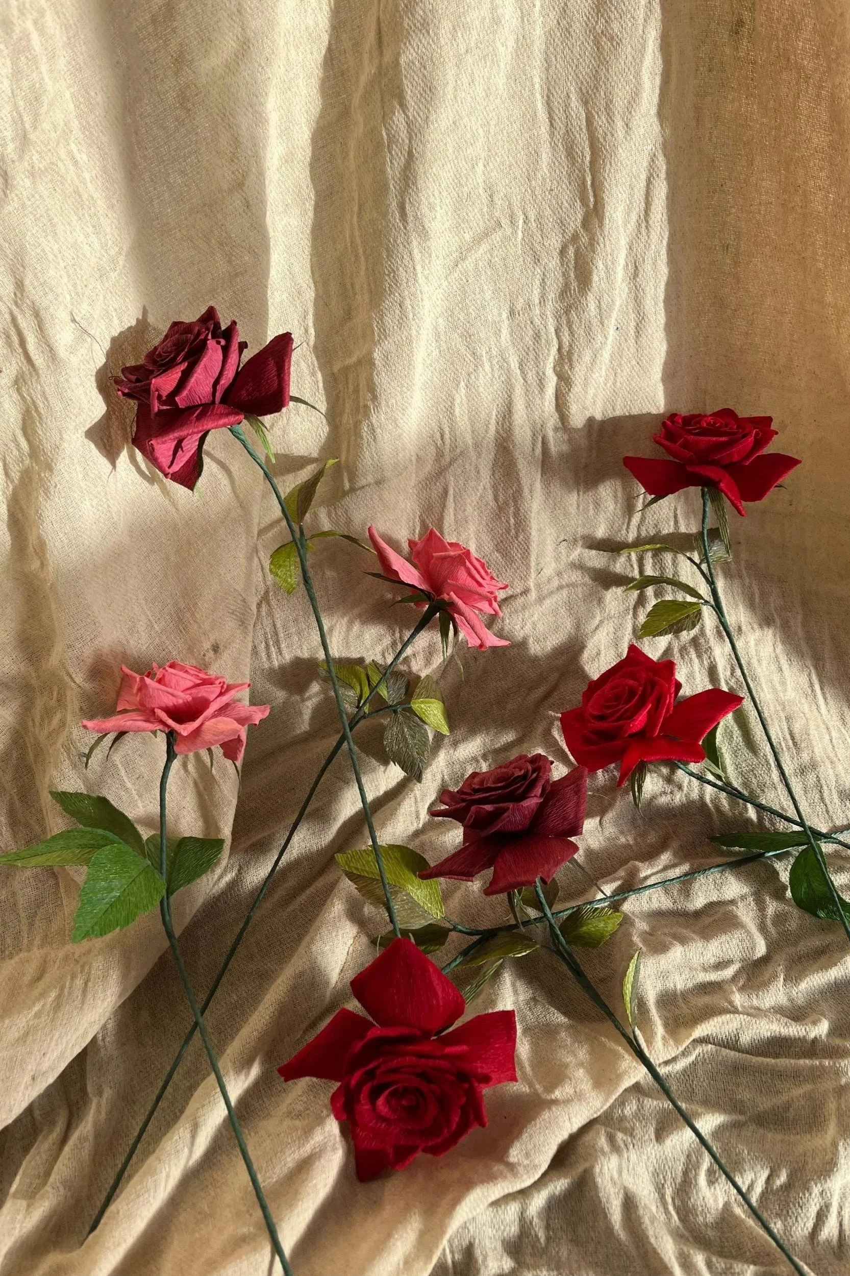 Collection of handmade paper roses in deep red and soft pink, arranged on linen fabric by Emmeli Kimhi