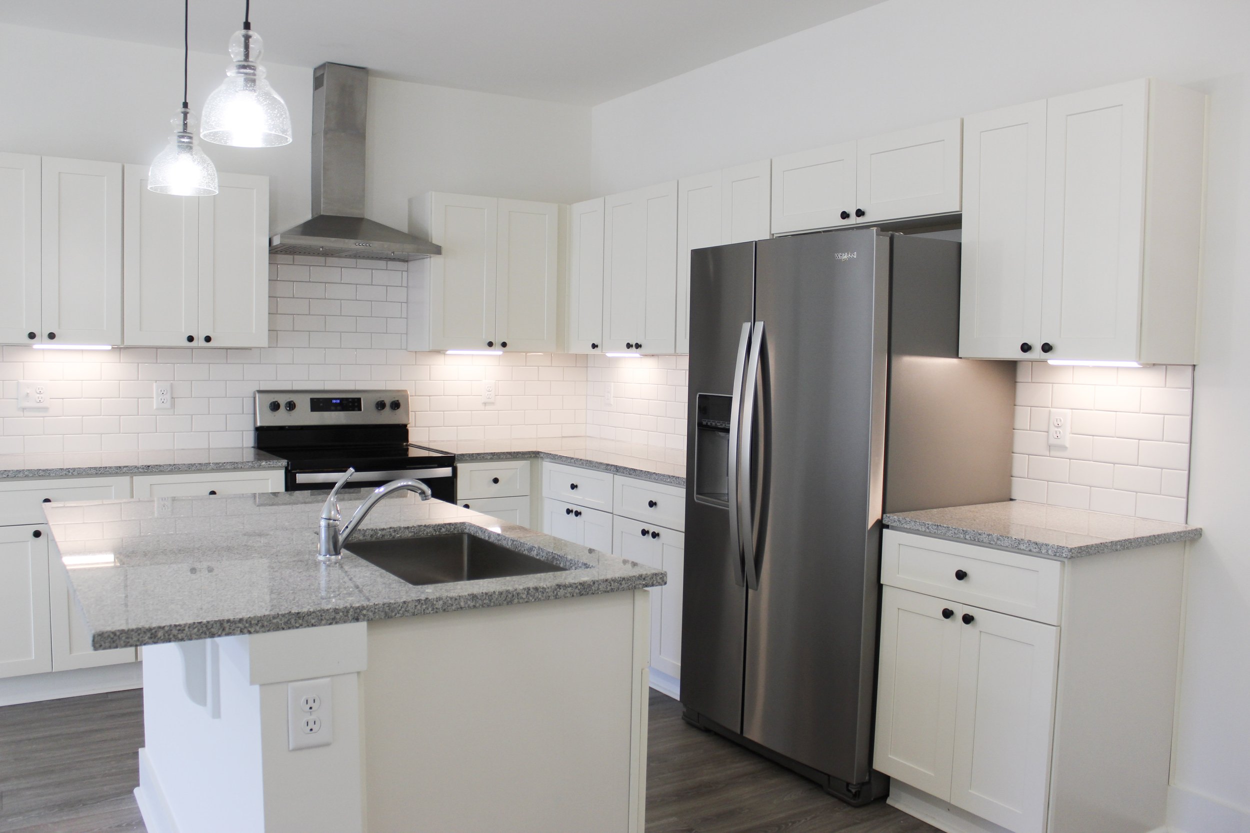 Modern kitchen with white cabinets, gray granite countertops, stainless steel refrigerator, black oven, and white subway tile backsplash.