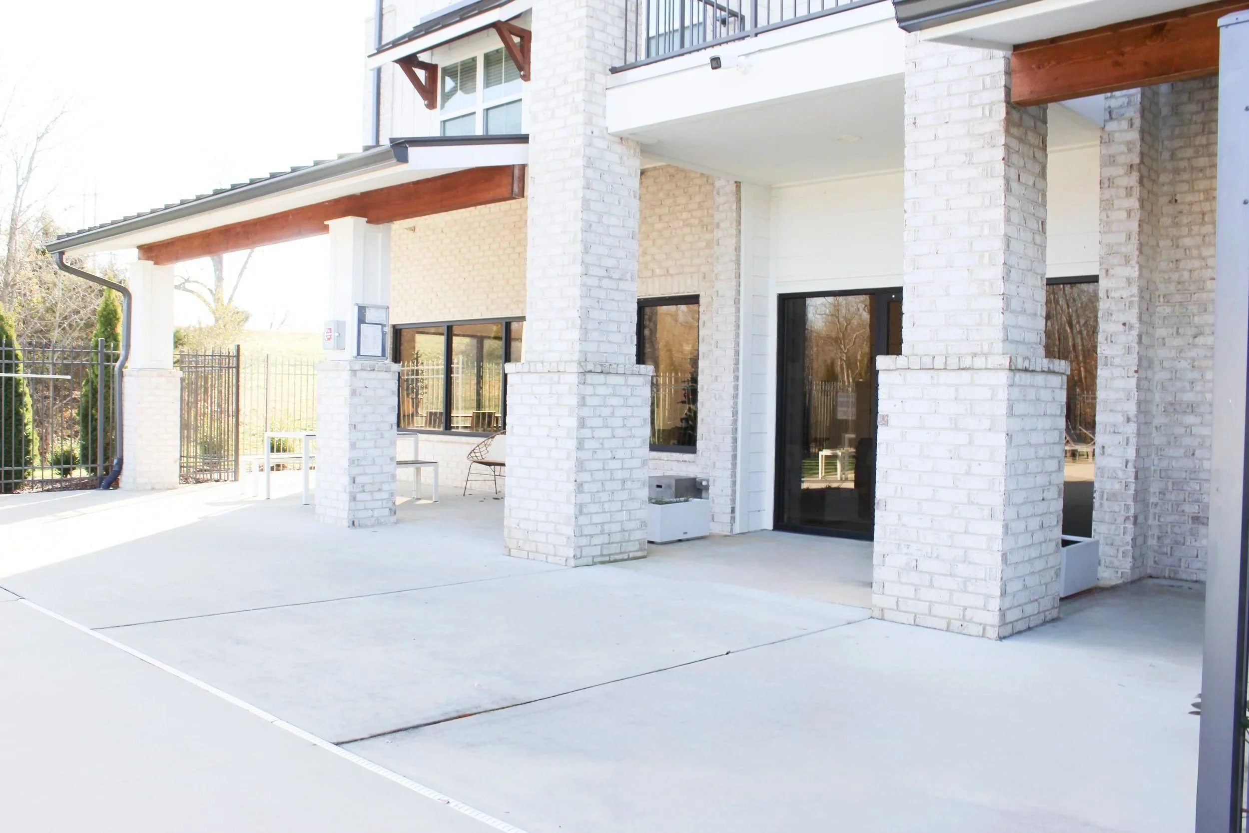 Outdoor patio with concrete flooring, white brick columns, black framed sliding glass doors, and outdoor furniture.