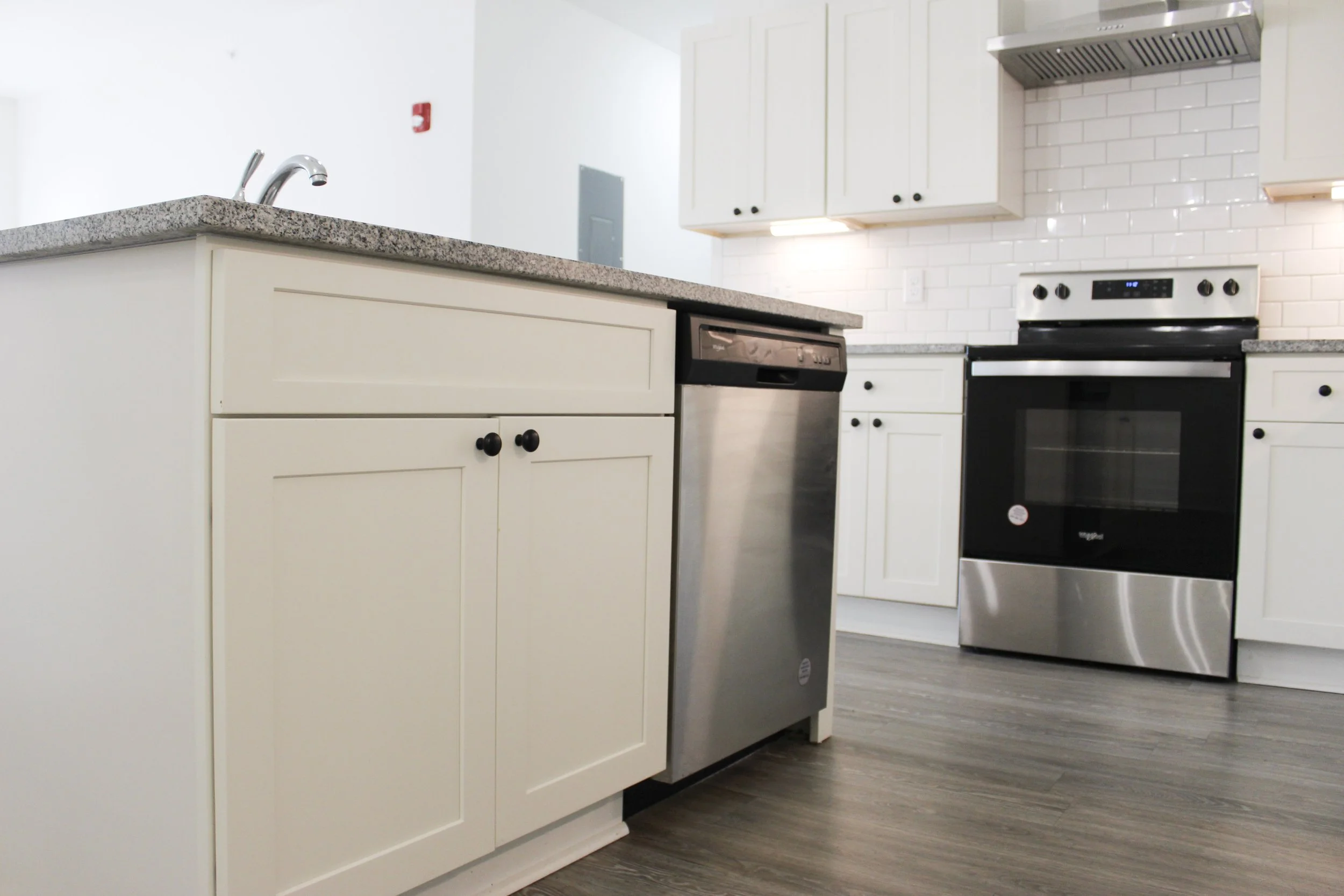 Modern kitchen with white cabinets, granite countertops, stainless steel appliances, and wood-look flooring.