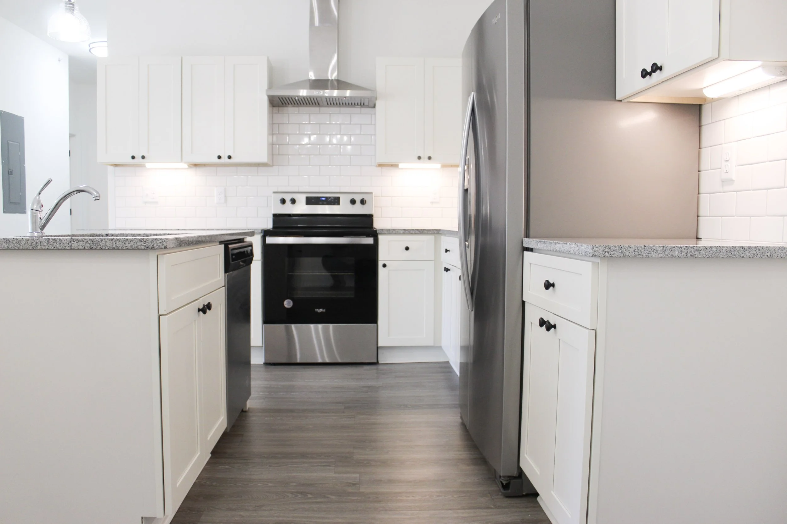 Modern kitchen with white cabinets, stainless steel appliances, white subway tile backsplash, and wood-look flooring.