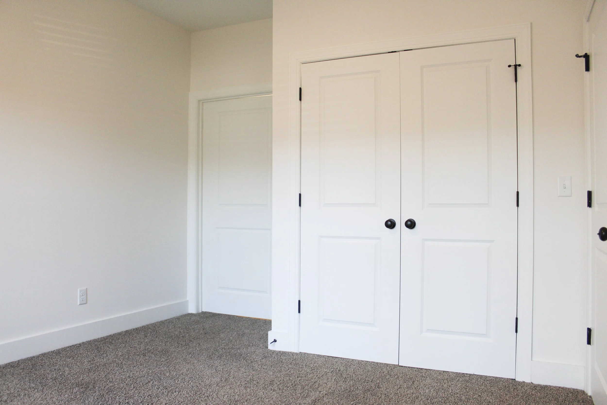 Empty room with white walls, closed closet doors, and beige carpet.