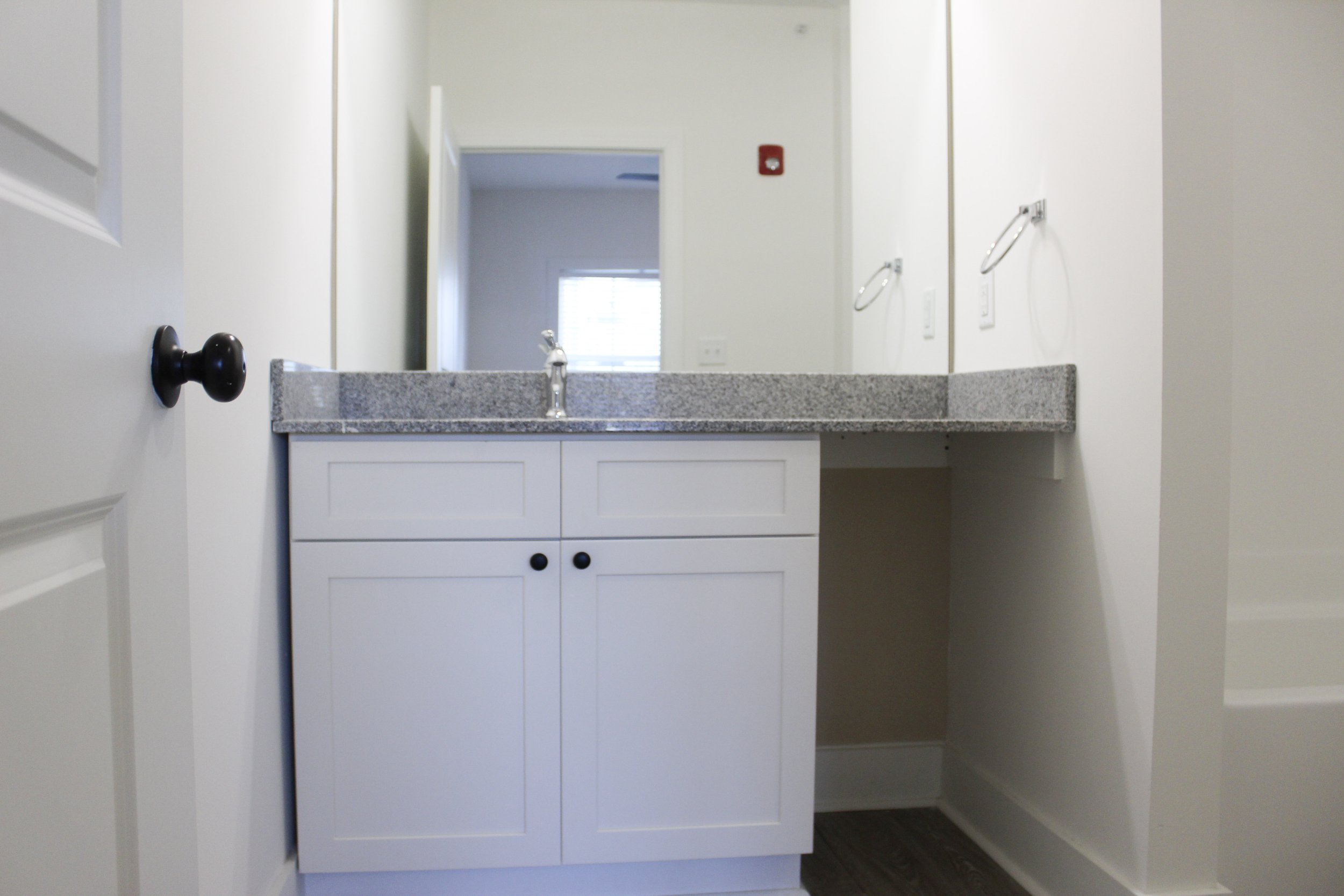 Empty bathroom vanity with a single faucet, a mirror above, white cabinet doors, and a gray countertop.