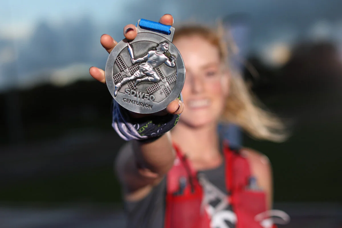 Laura, sleep specialist, occupational therapist, CBTi therapist smiling holding a silver medal for completing Centurion 50 mile race