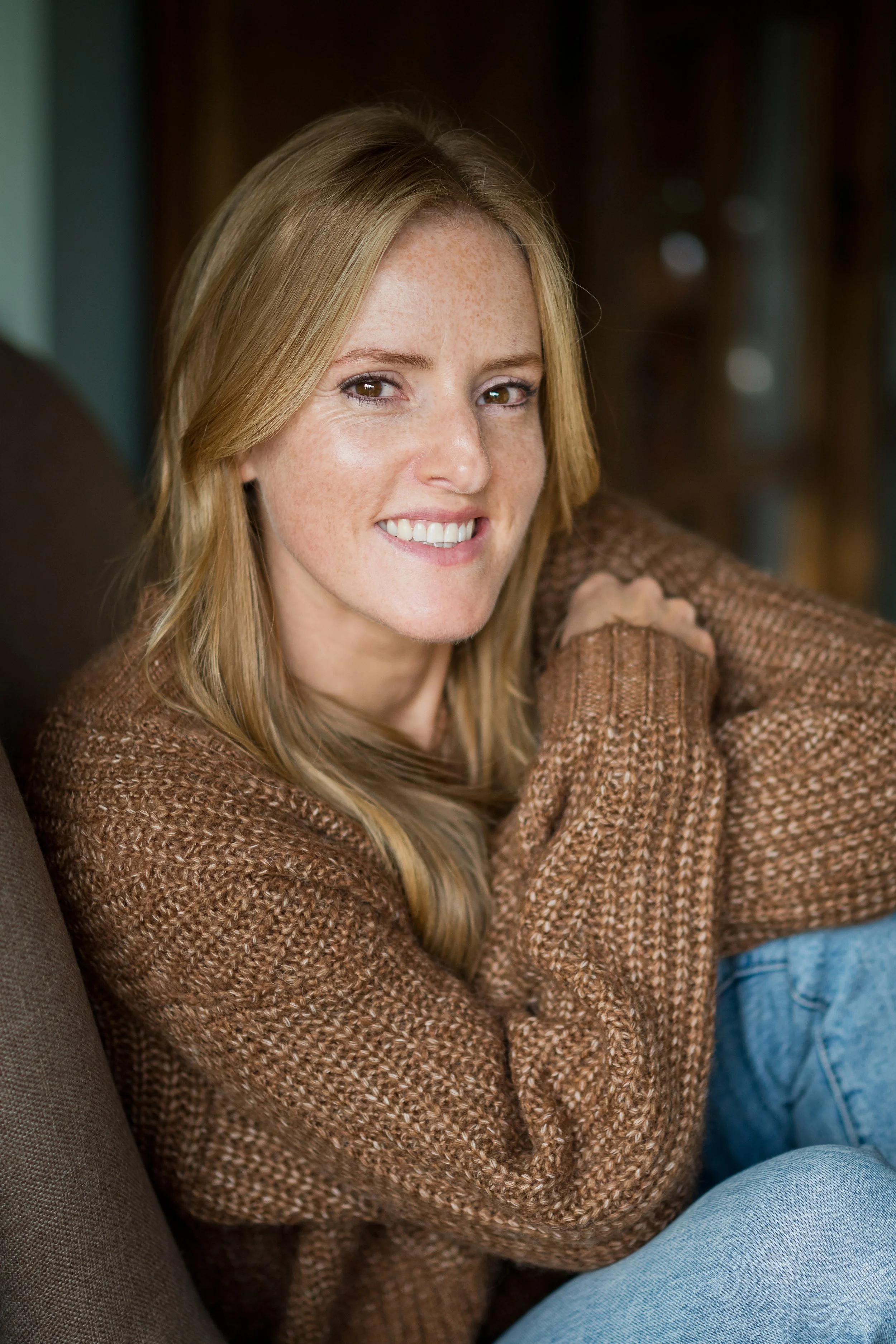 Laura sitting on chair arms crossed smiling warm and friendly