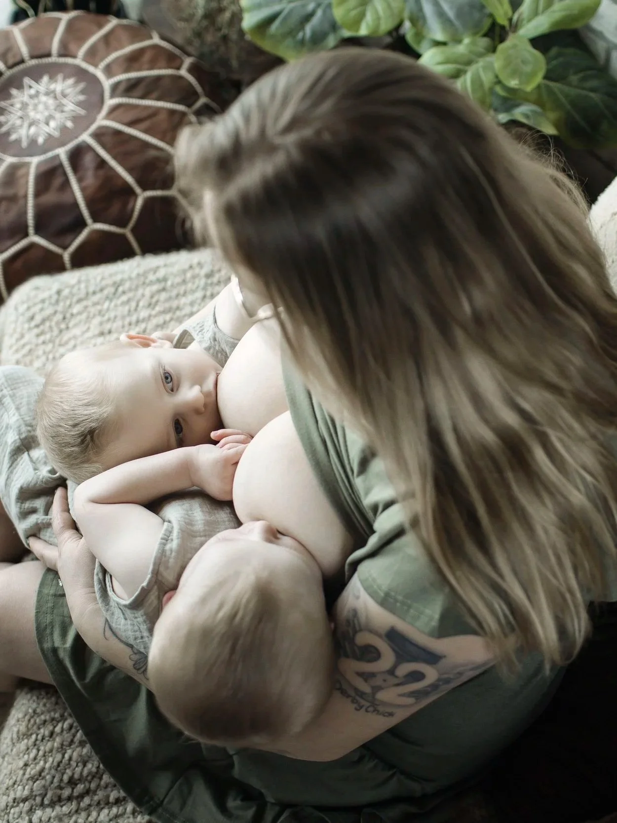 A woman is breastfeeding two babies simultaneously, one on each side, while sitting on a couch.
