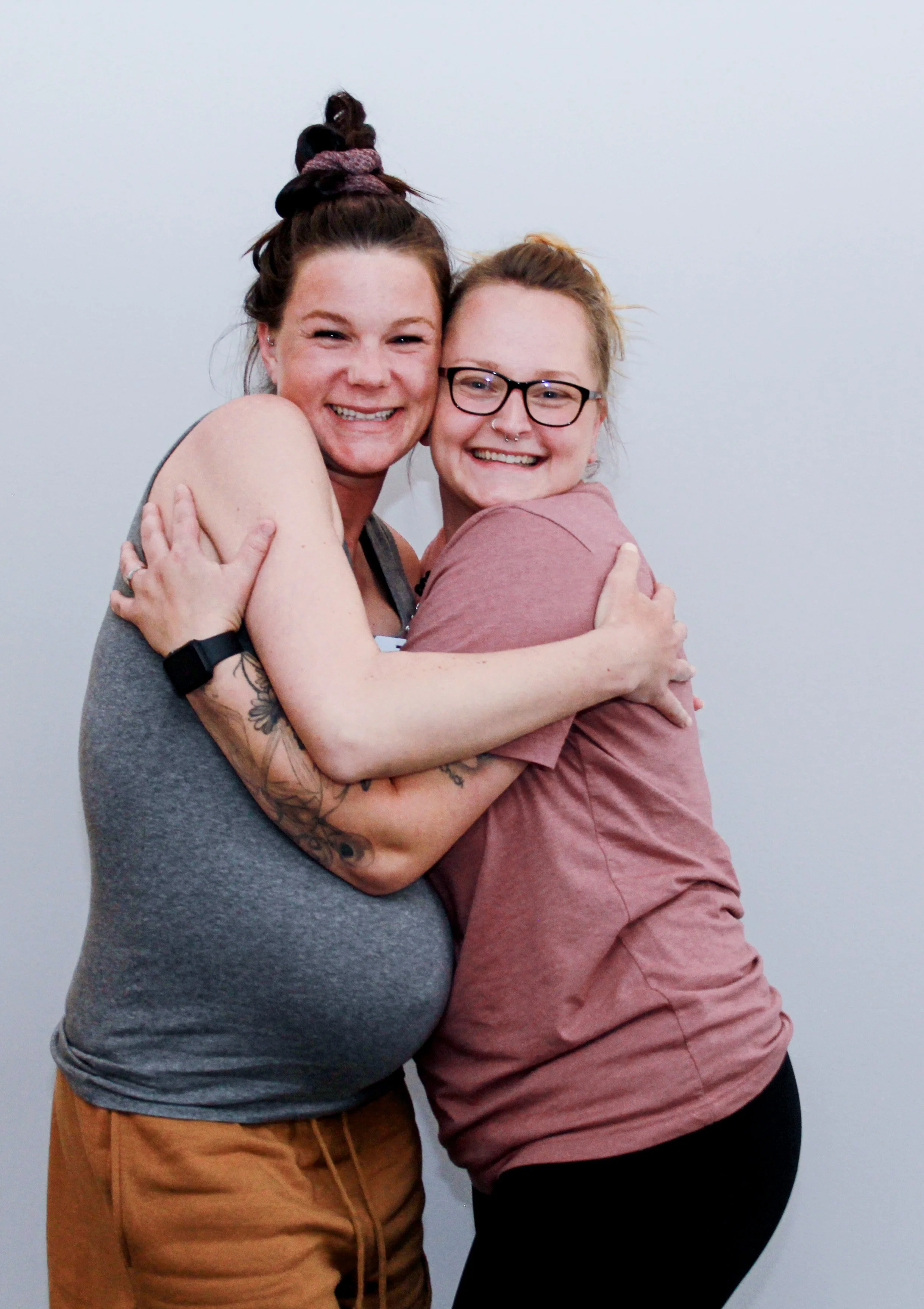 Two women hugging and smiling at the camera against a plain background.