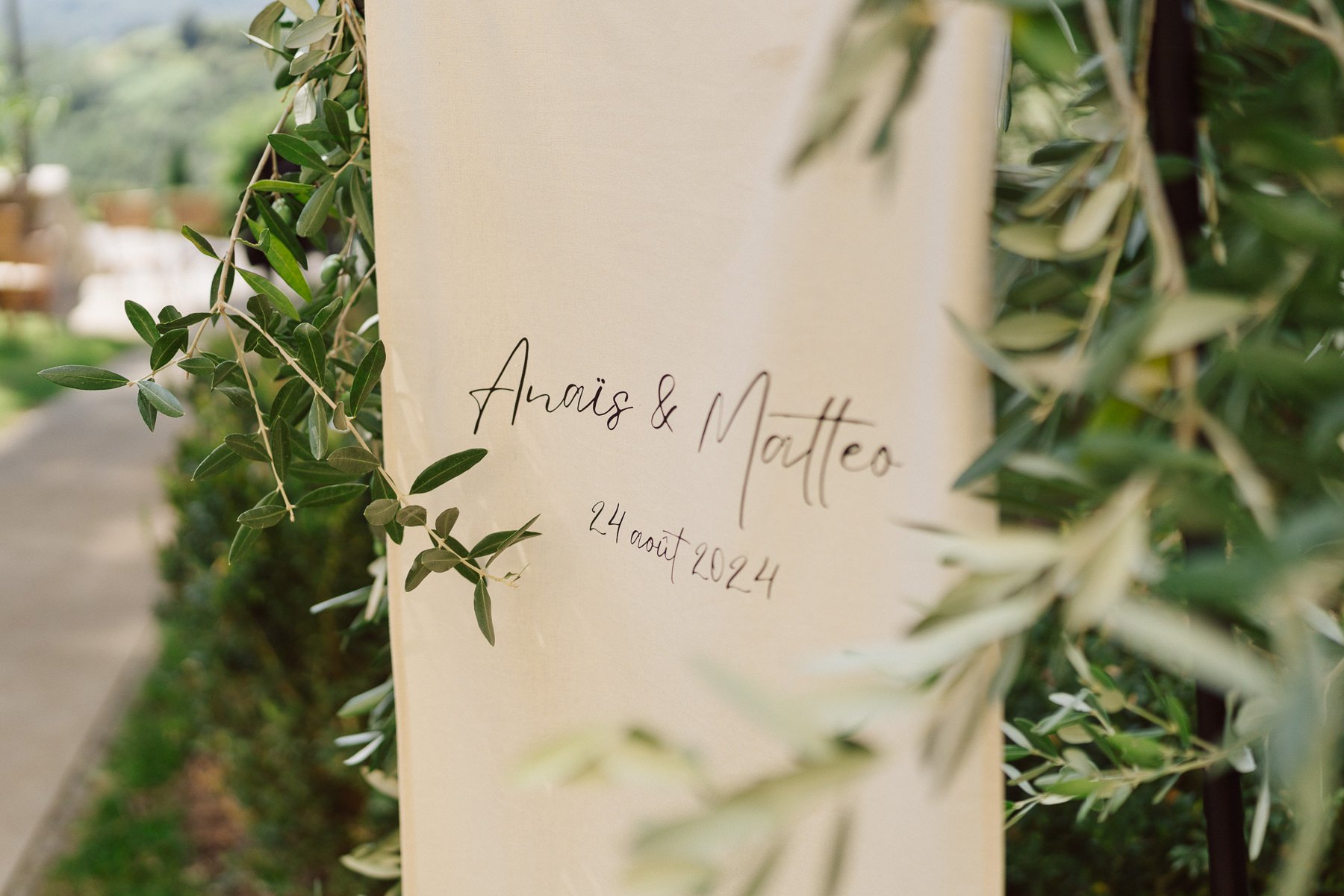 Panneau de mariage avec les prénoms Anaïs et Matteo et la date, décoré de feuillage d’olivier en Toscane