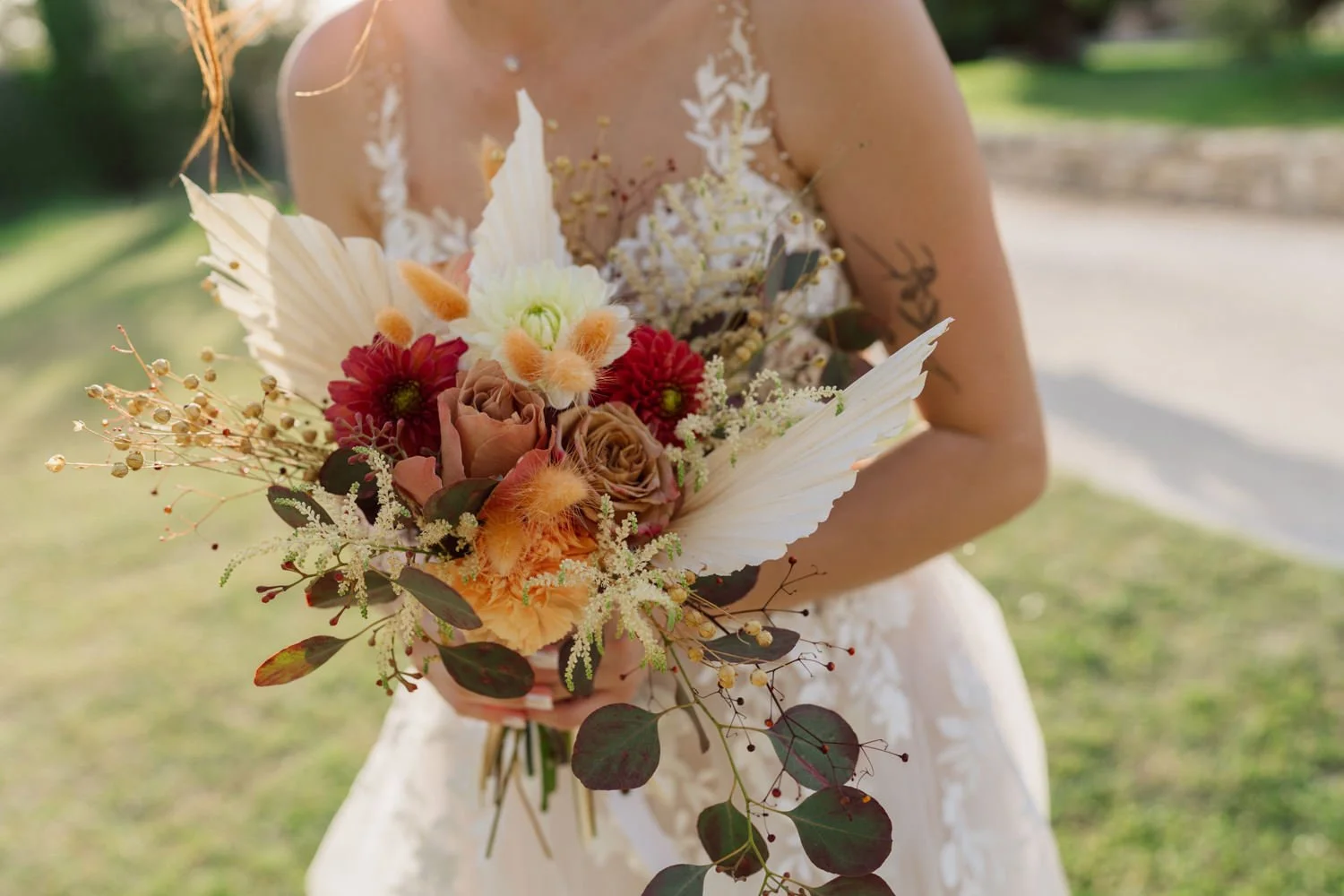 Gros plan sur un bouquet de mariée bohème composé de fleurs séchées, tons terracotta, crème et bordeaux.