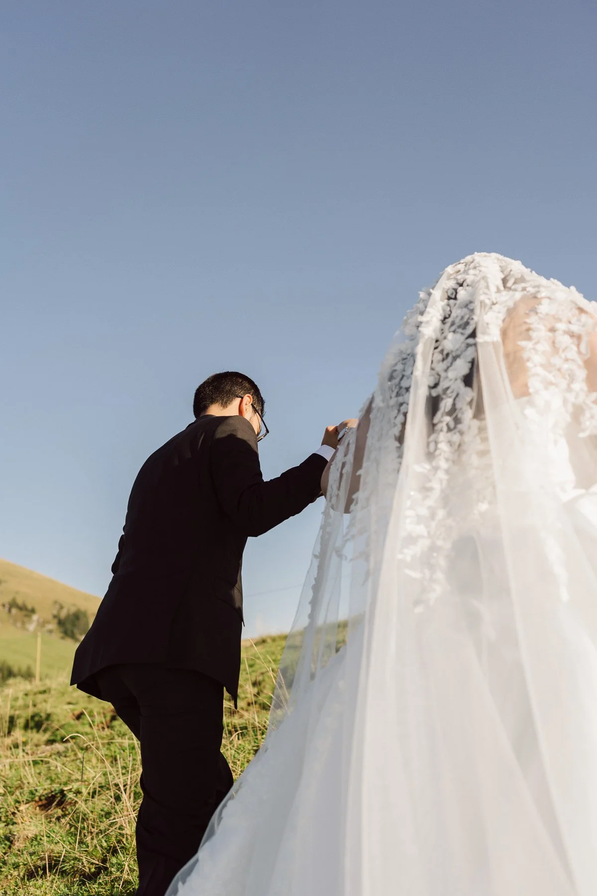 Couple de mariés marchant main dans la main en montagne en Suisse, voile de mariée et robe longue – photo romantique mariage par Nonante Émotions
