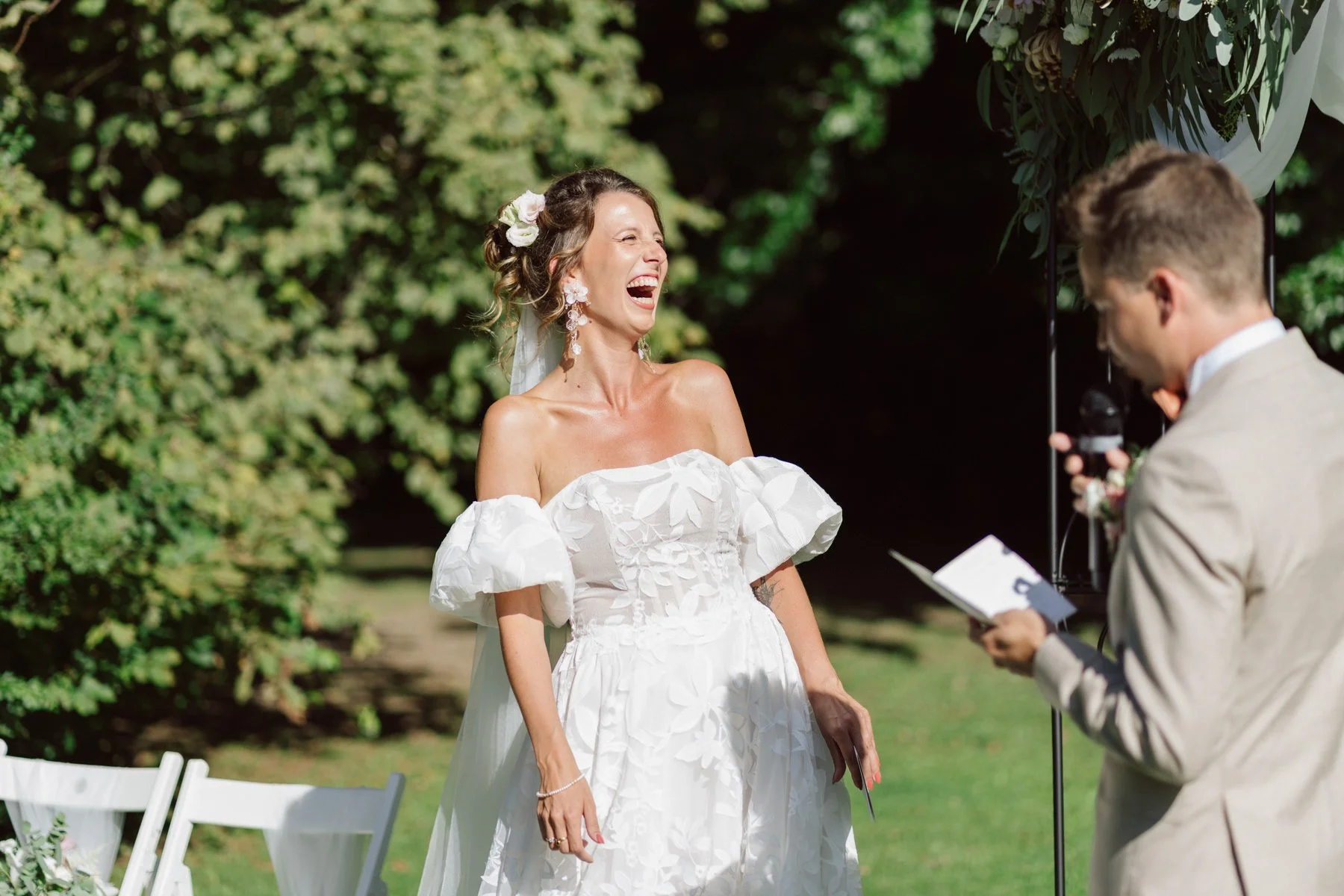 La mariée éclate de rire pendant la cérémonie laïque en extérieur au Castel de Bois-Genoud, face au marié lisant ses vœux