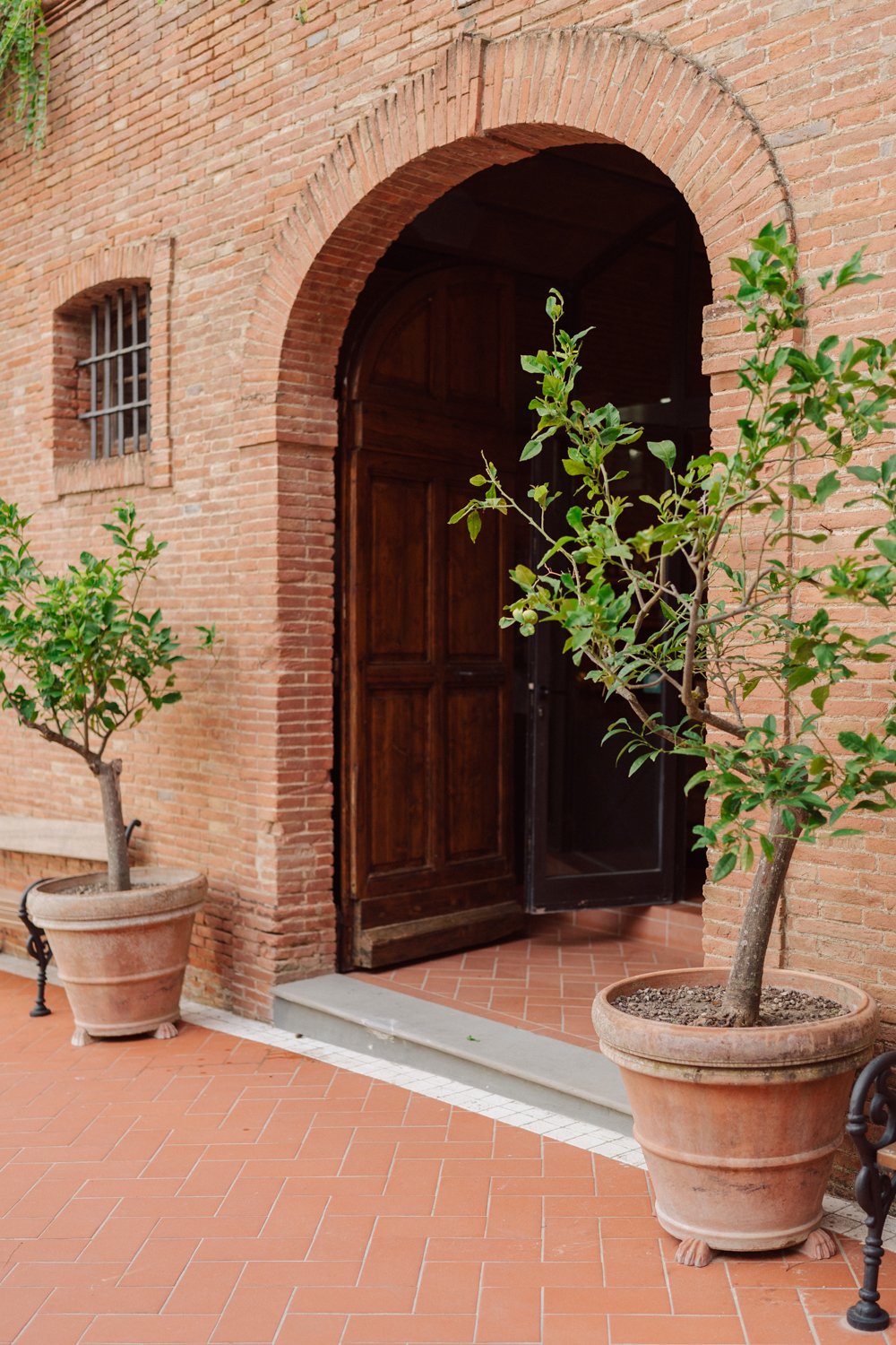 Entrée d’une villa toscane avec arche en brique, porte en bois et pots en terre cuite
