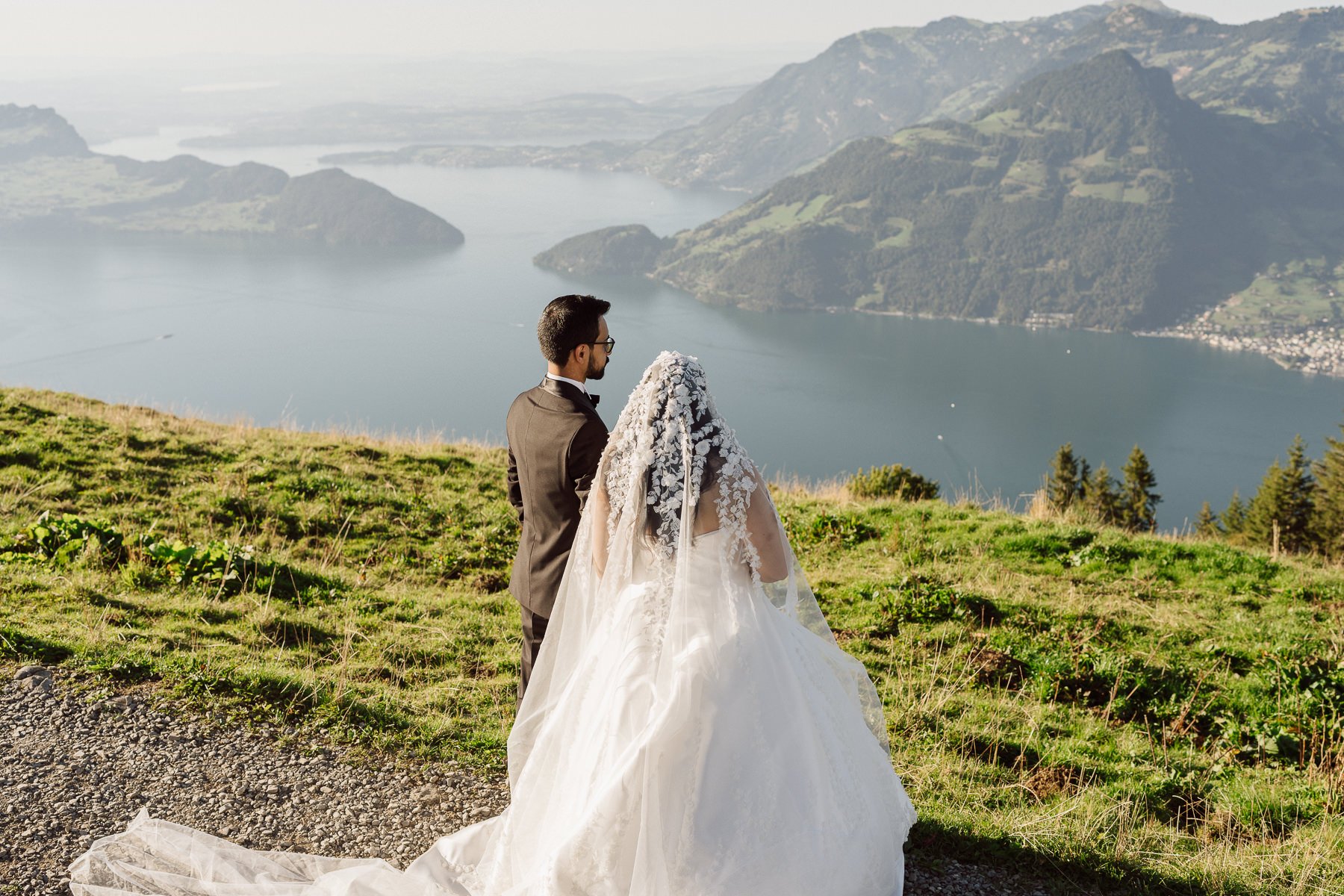 Mariés de dos contemplant un lac et les montagnes suisses depuis un sommet alpin – photo de couple mariage par Nonante Émotions