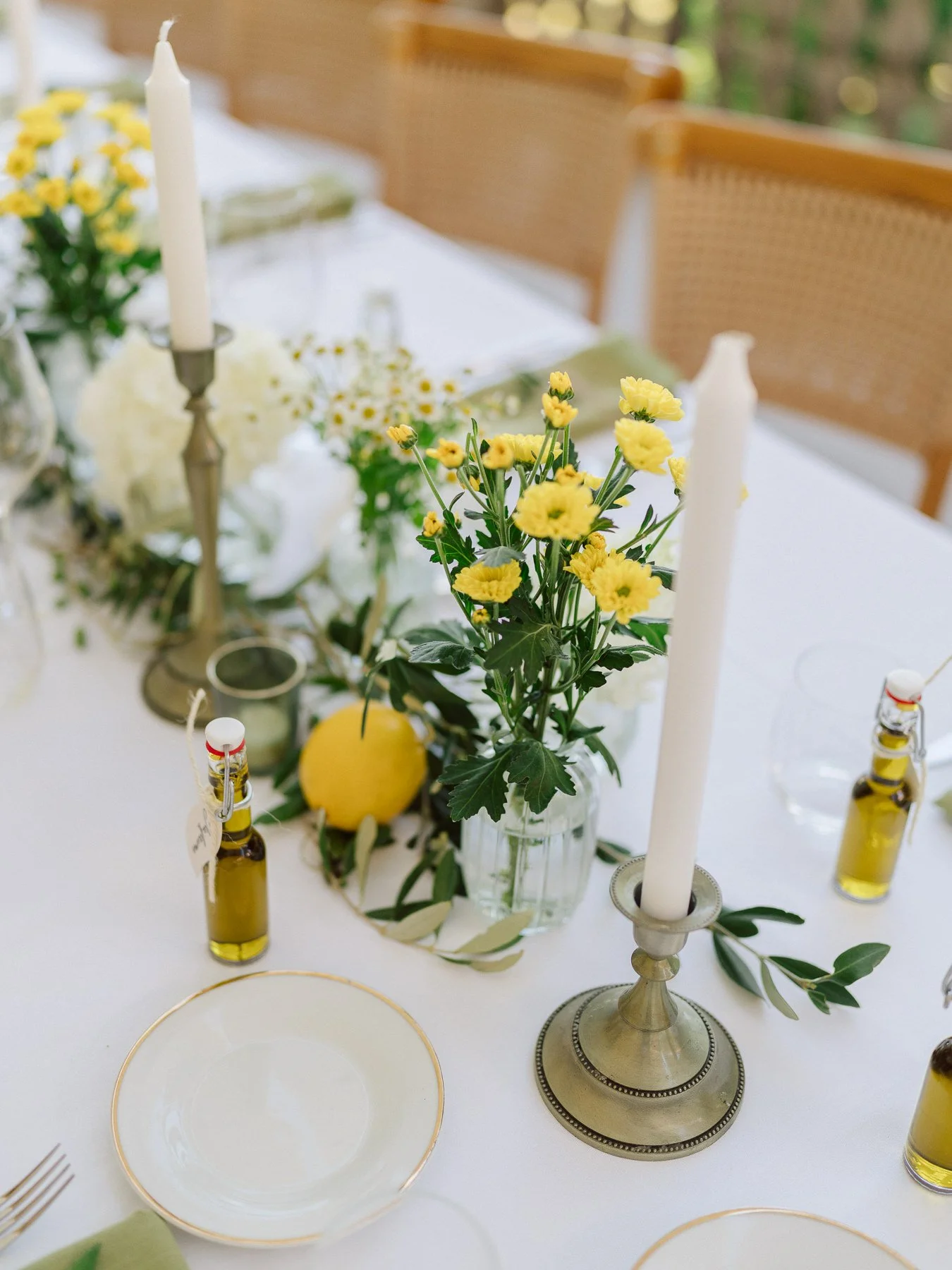 Décoration de table de mariage en Toscane avec bougies blanches, fleurs jaunes, citron et branches d’olivier sur une nappe blanche élégante.